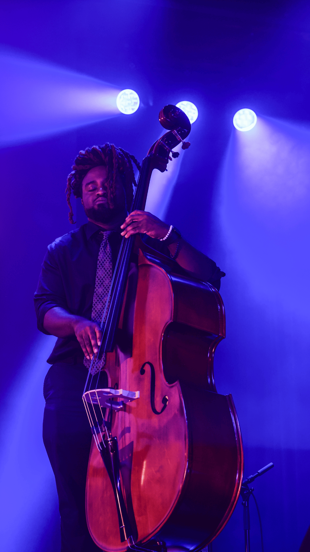 Musician playing upright bass on stage under blue stage lights