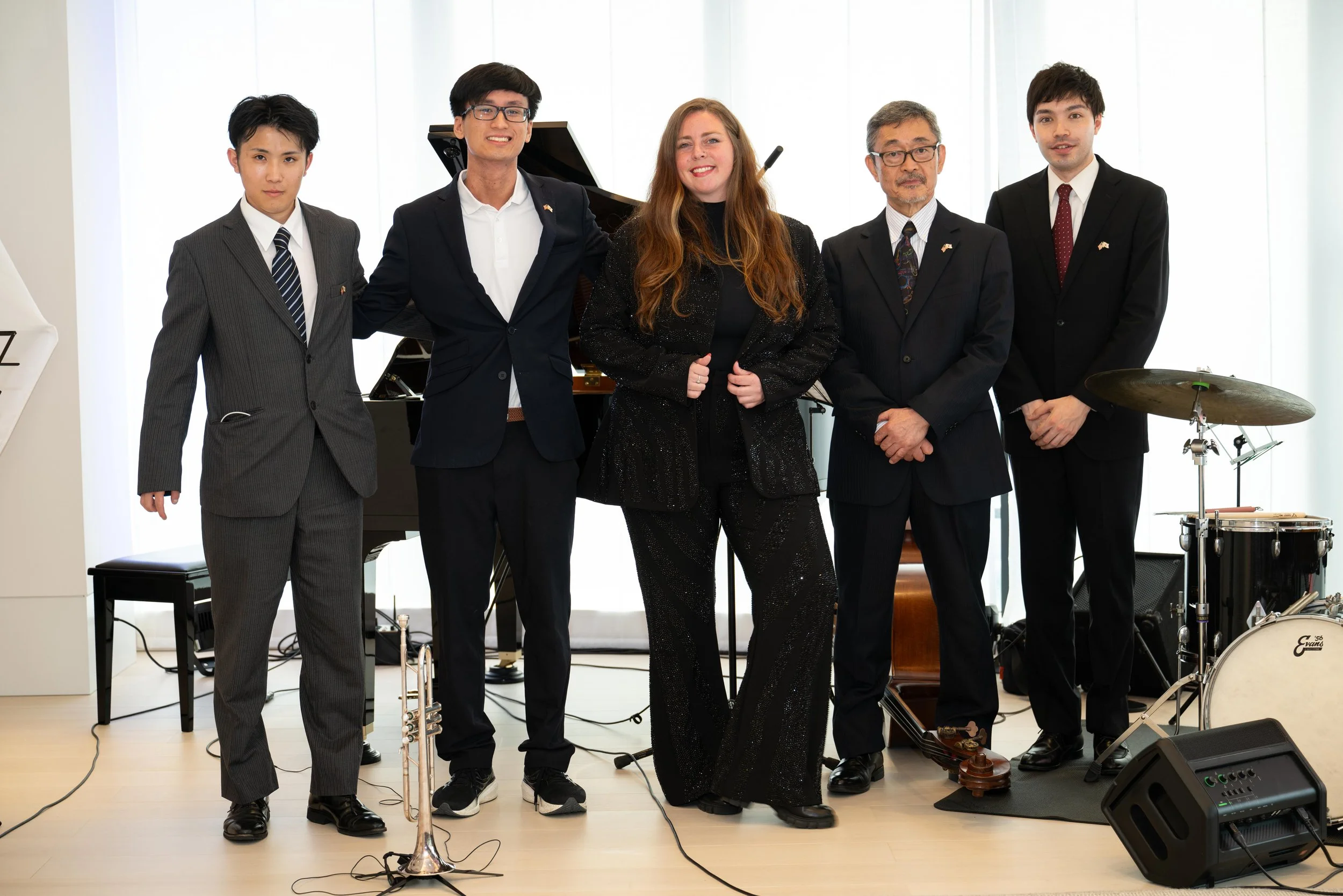 Group of five musicians in formal attire posing with musical instruments indoors.