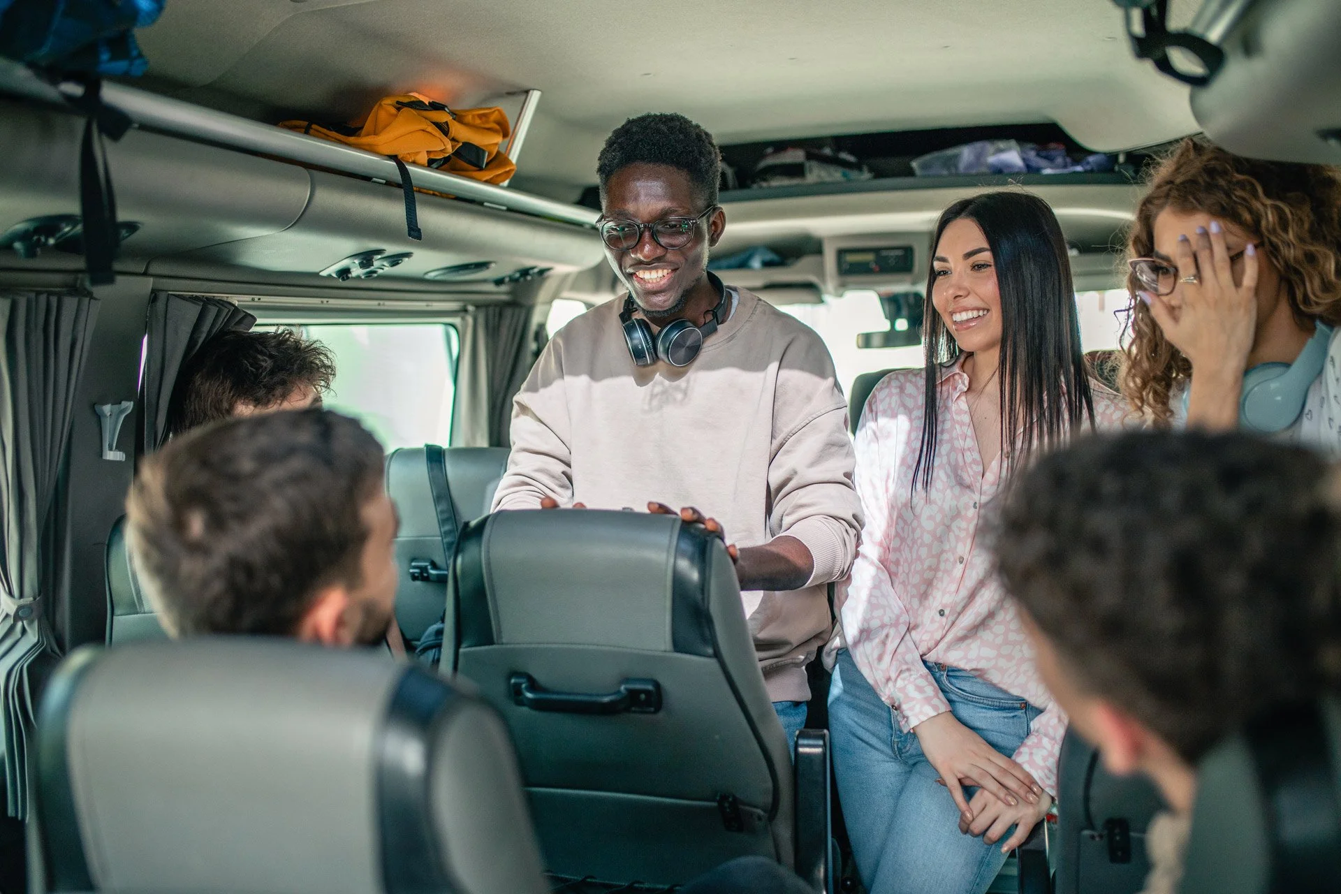 Smiling group of diverse young adults sitting and standing inside a bus, engaging in conversation.