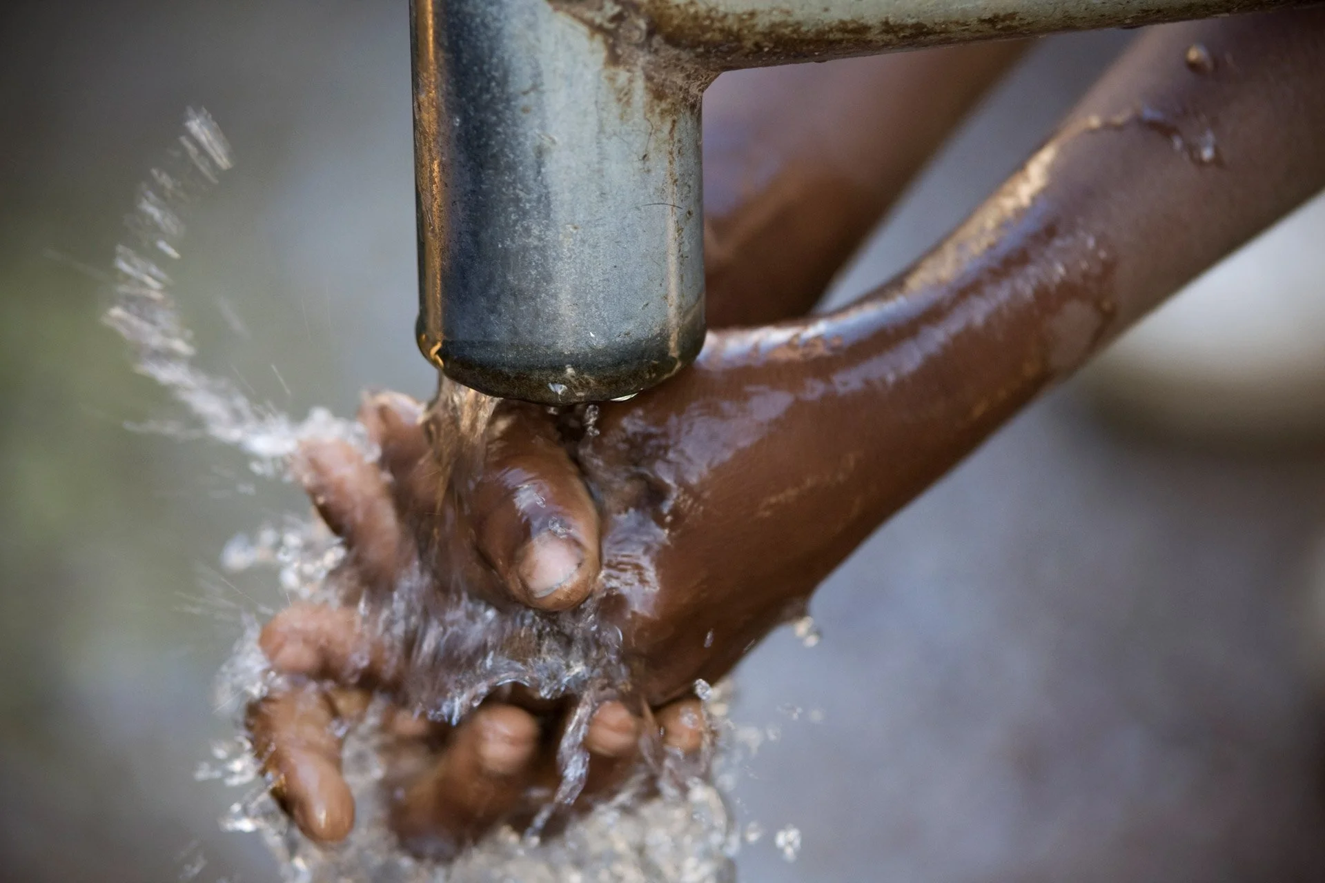 Close-up of a hand under a water fountain, water splashing as the person rinses or washes their hand.