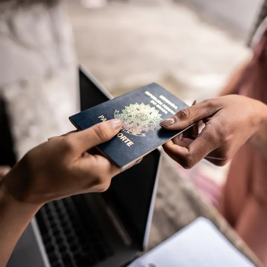 A person receiving a colorful passport from another person in front of a laptop.