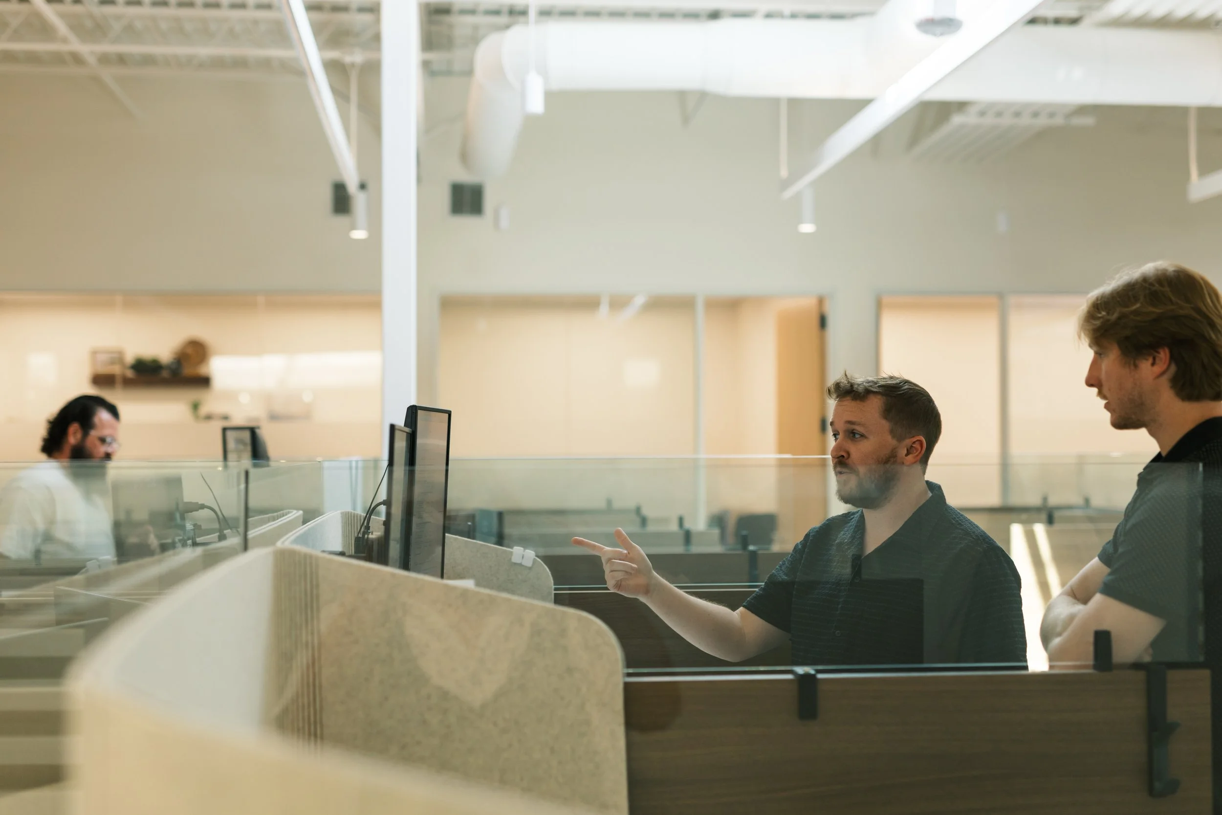 Office workers sitting at desks in a modern open-plan office engaged in conversation.