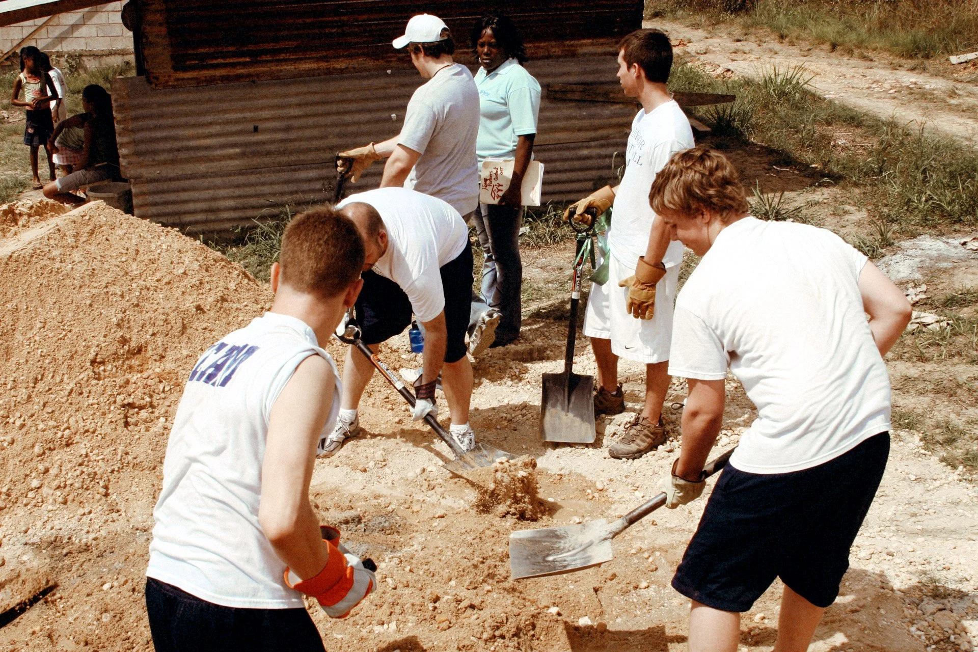 Group of young volunteers digging and working together on a construction project outdoors, with some holding shovels and wearing gloves.
