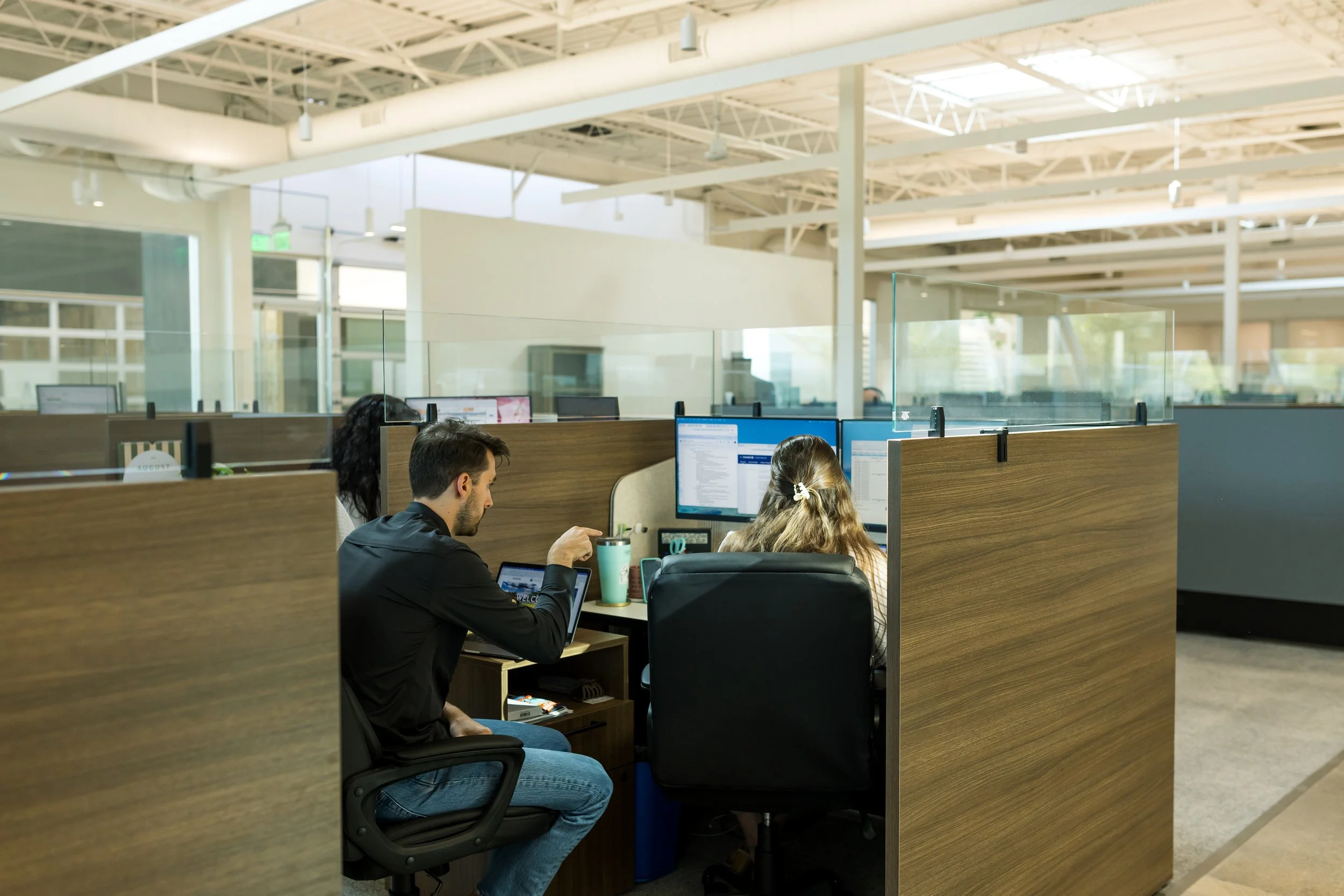 People working at computers in an open office space with high ceilings and bright lighting.
