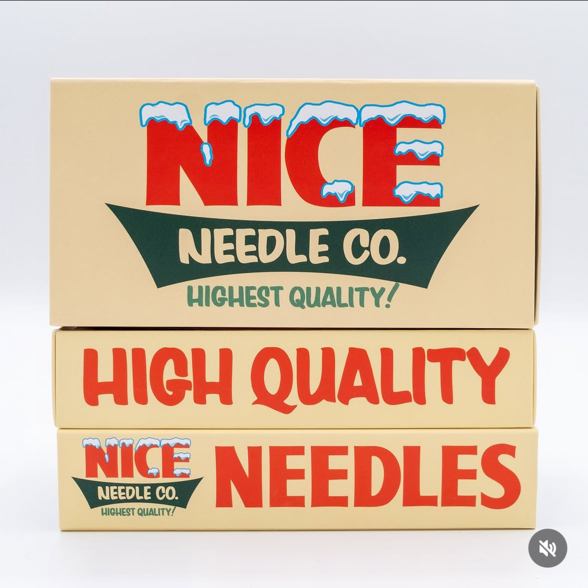 Stack of boxes labeled with colorful text. The top box reads "NICE NEEDLE CO. HIGHEST QUALITY!" with snow cap designs on the word "NICE." The middle box says "HIGH QUALITY" in large red letters. The bottom box repeats "NICE NEEDLE CO. HIGHEST QUALITY!" with similar snow cap designs.