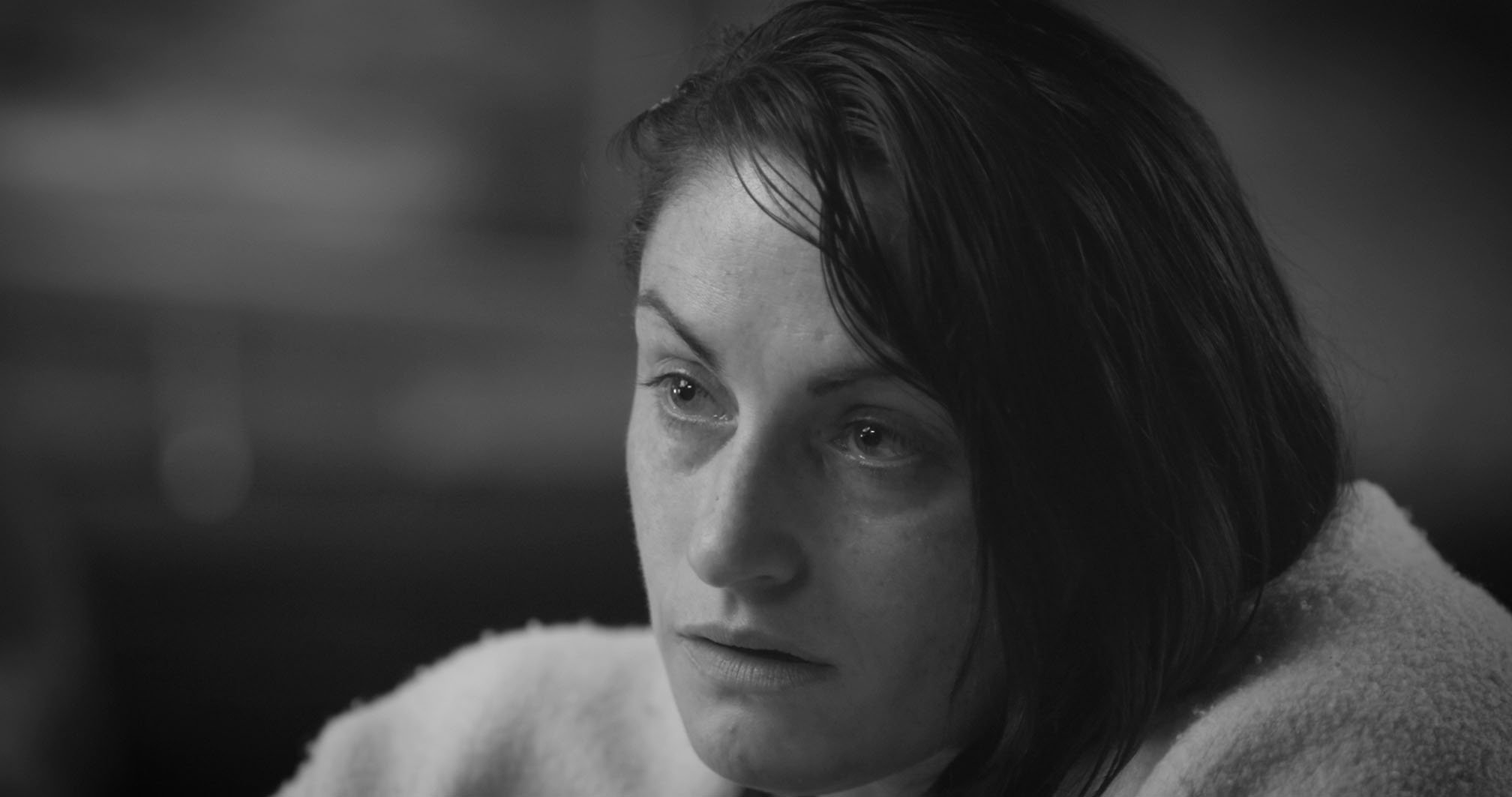 Close-up black and white photo of a woman with wet, dark hair and a contemplative expression, looking slightly downward.