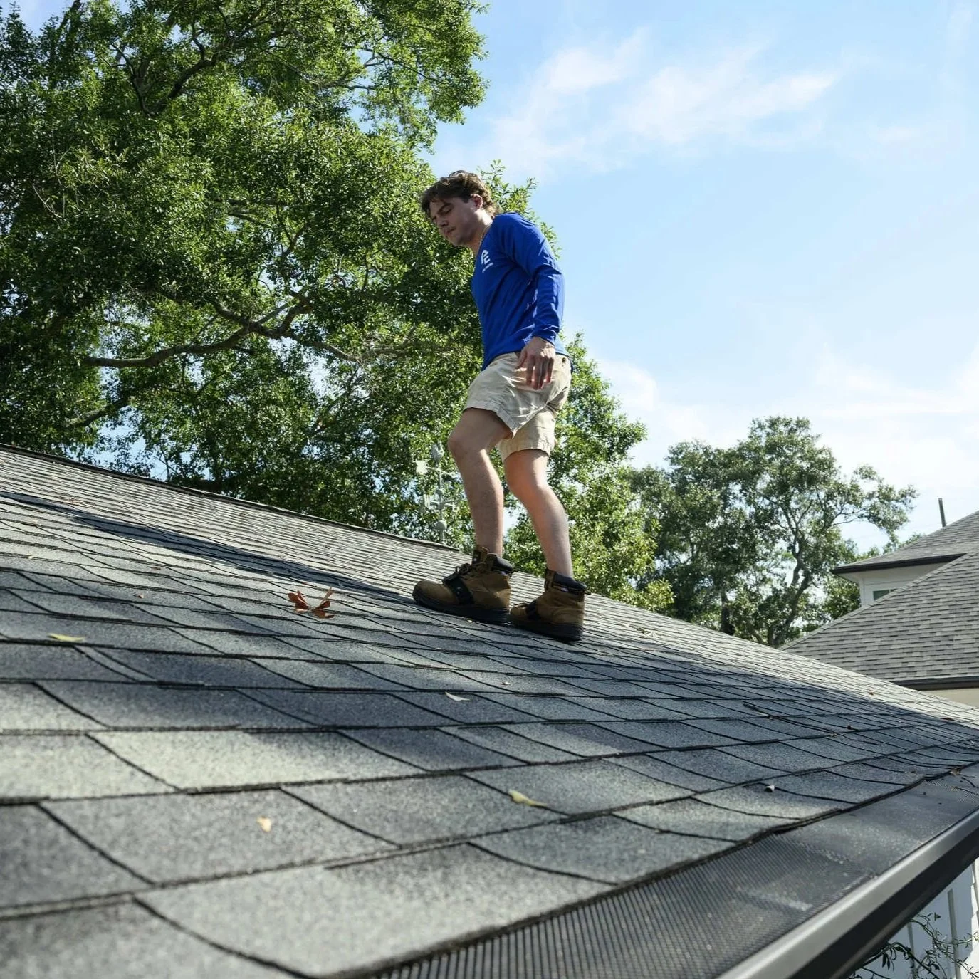 Professional roofer walking on asphalt shingle roof while inspecting residential roofing system for damage, wear, and maintenance requirements.