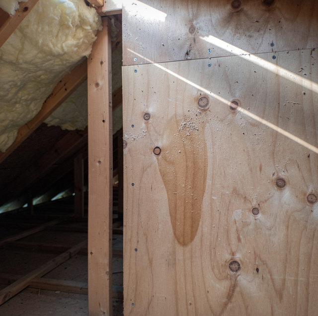 A workbench with plywood surface and sawhorse supports holds a caulking gun and gloves in an open garage with ladder and wood