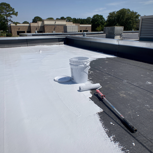 roller applying white elastomeric roof coating to flat roof