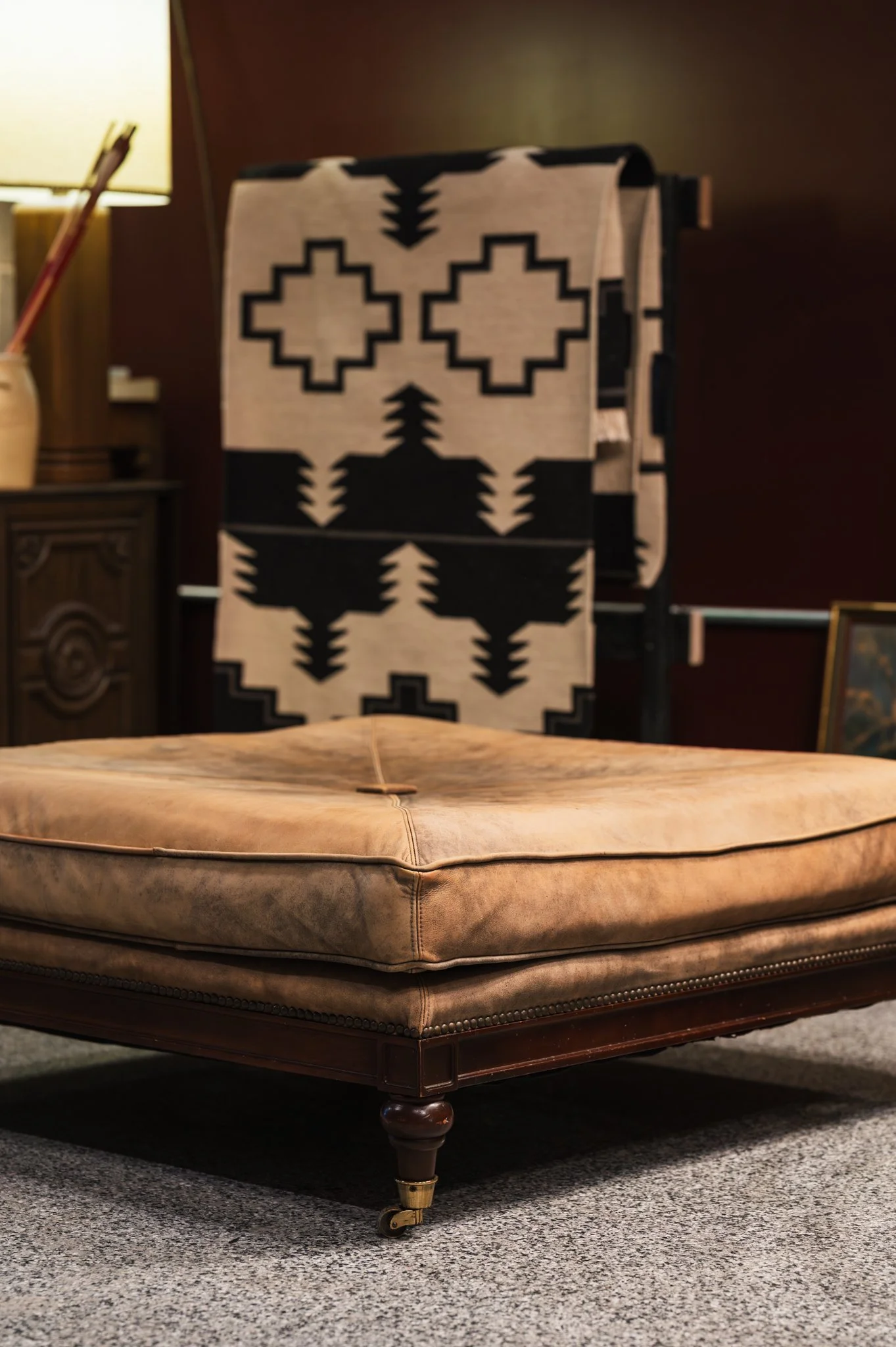Close-up of a vintage leather ottoman with studded trim on a carpeted floor.