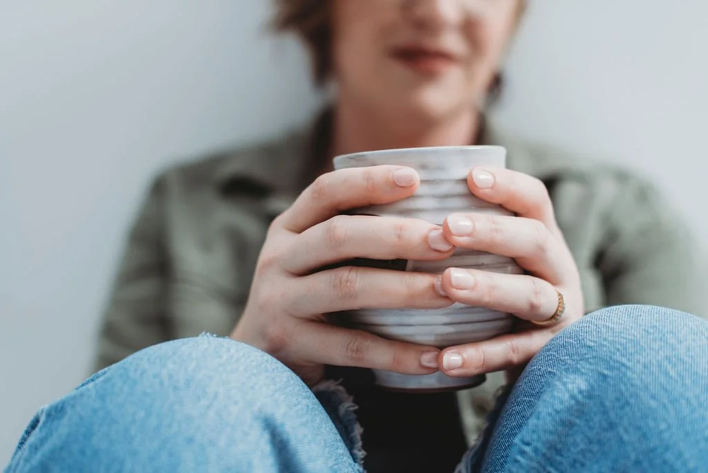 Hands holding a warm ceramic mug during a collaborative business coaching conversation about thoughtful decision-making and sustainable entrepreneurship.
