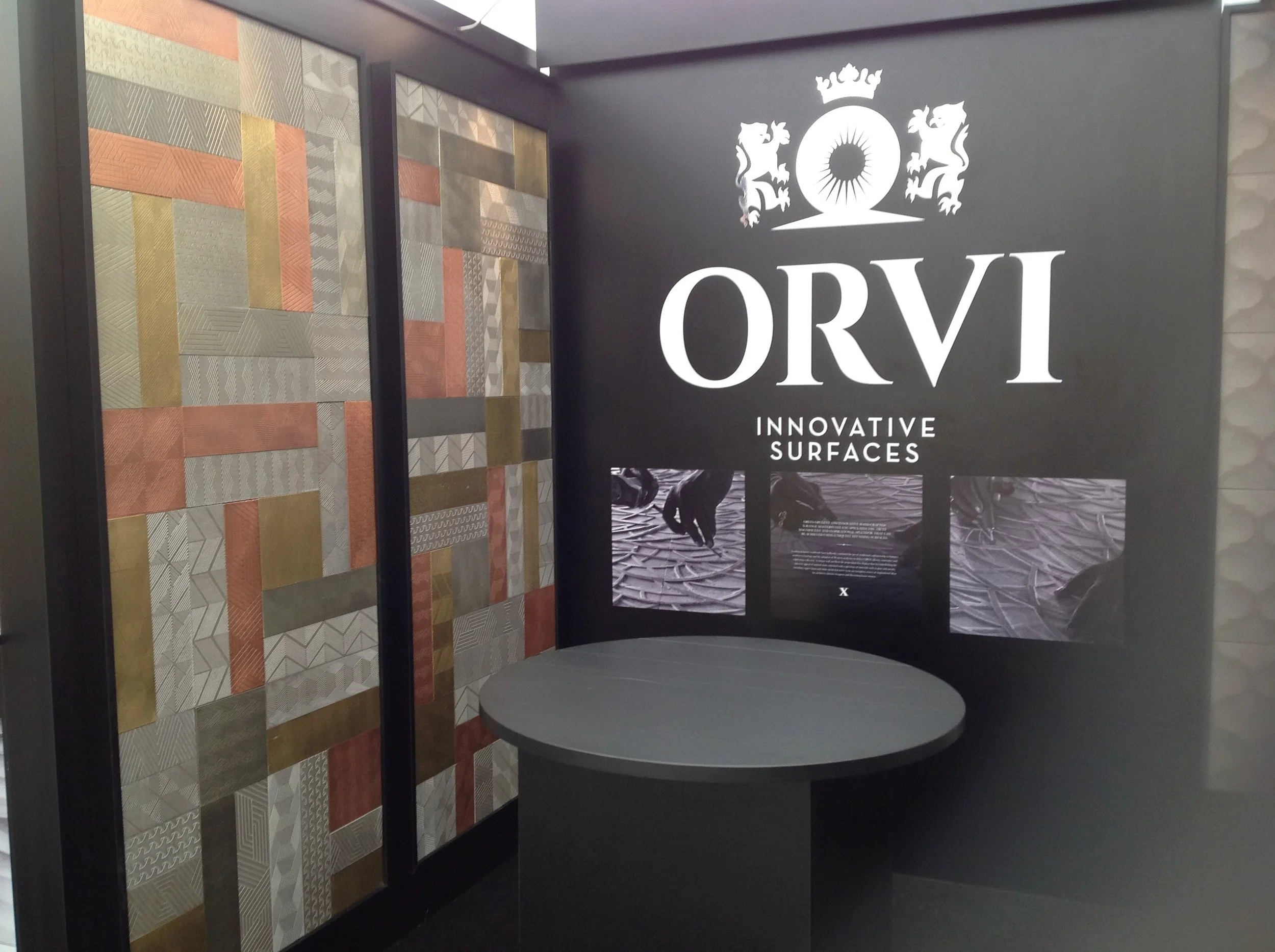 Display booth for Orvi Innovative Surfaces featuring textured wall panels, a round table, and branding signage.