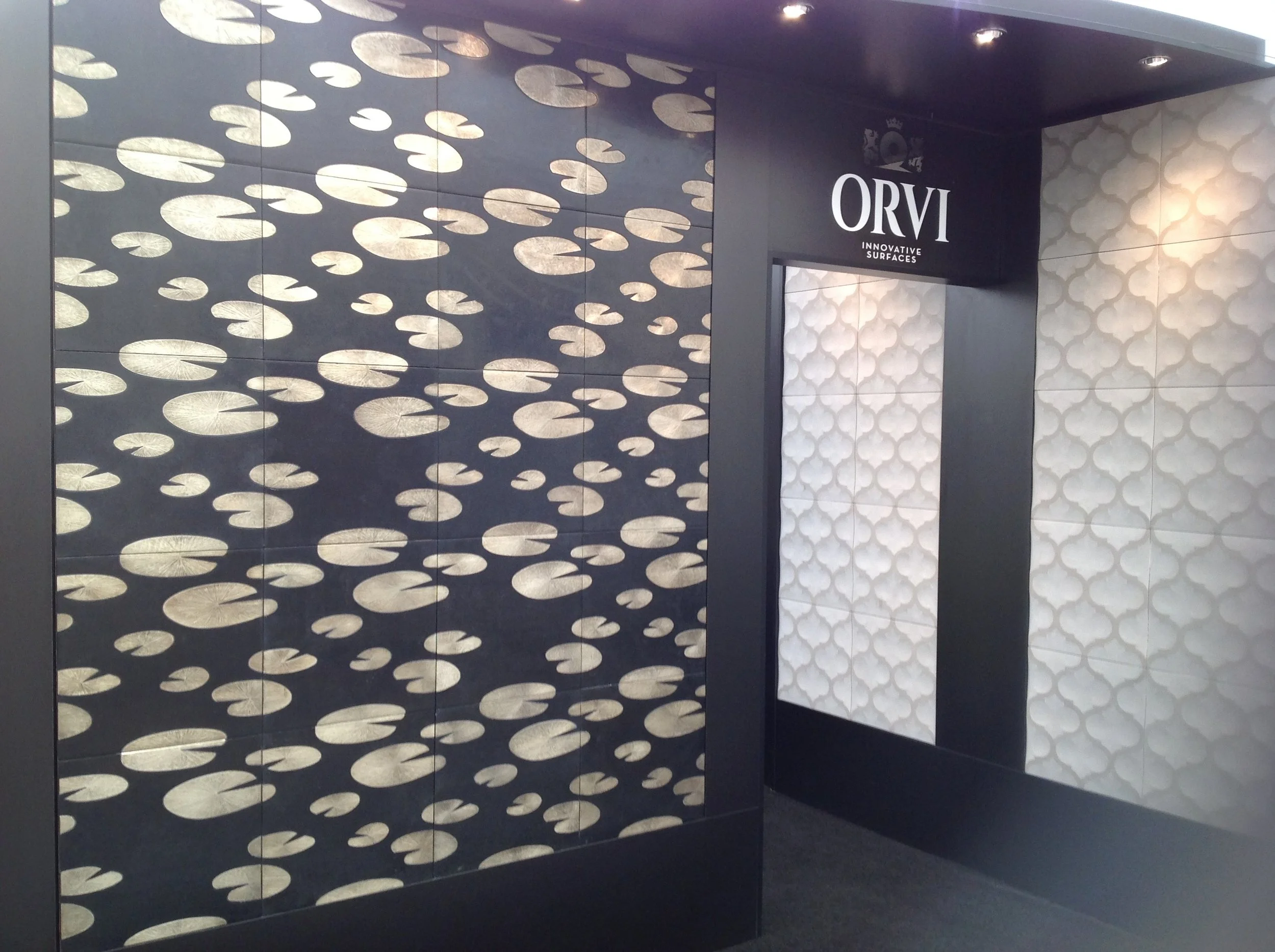 Decorative wall panels with abstract patterns, featuring a black background and gold circular designs, alongside white textured panels with the Orvi logo overhead.