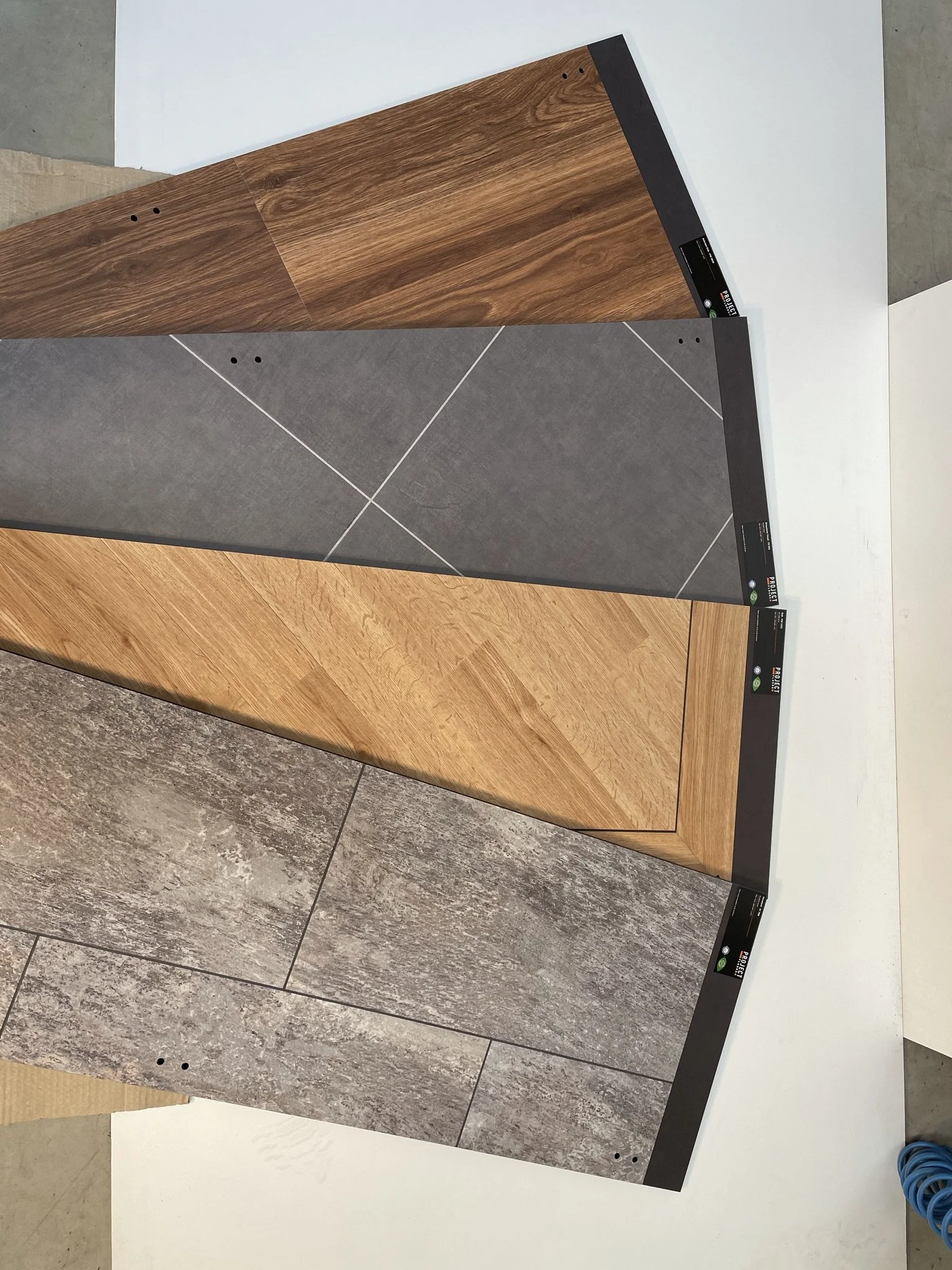 Four different flooring samples overlapping on a flat surface. The samples include various styles such as wood grain and stone tile patterns.
