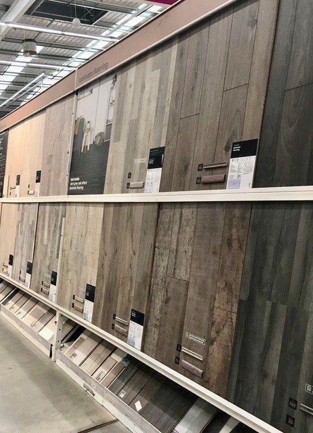 Display of laminate flooring samples in various wood finishes at a store, showing different colors and textures.