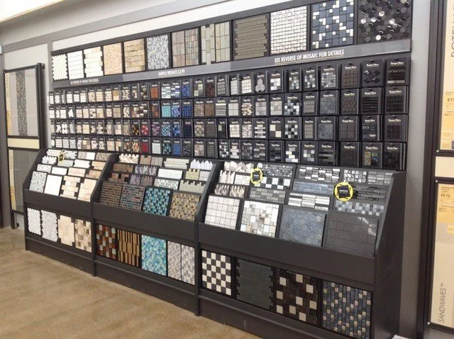 A display of various mosaic tiles on a store wall, organized by color and style, showcasing options for flooring or wall decoration.