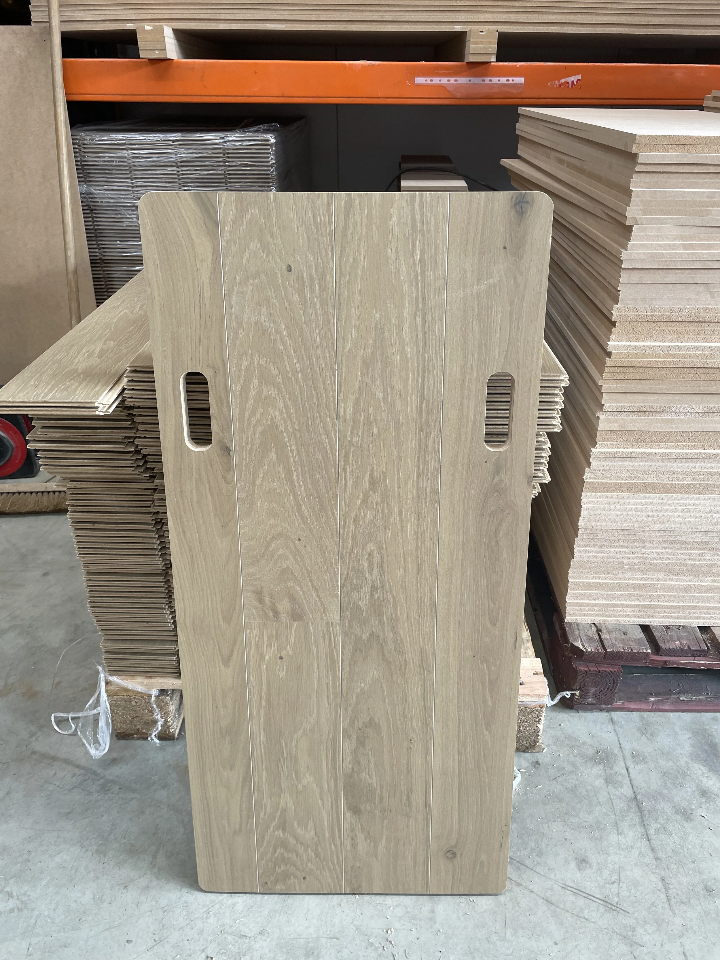 Stack of wooden panels with cut-out handles in a warehouse setting.