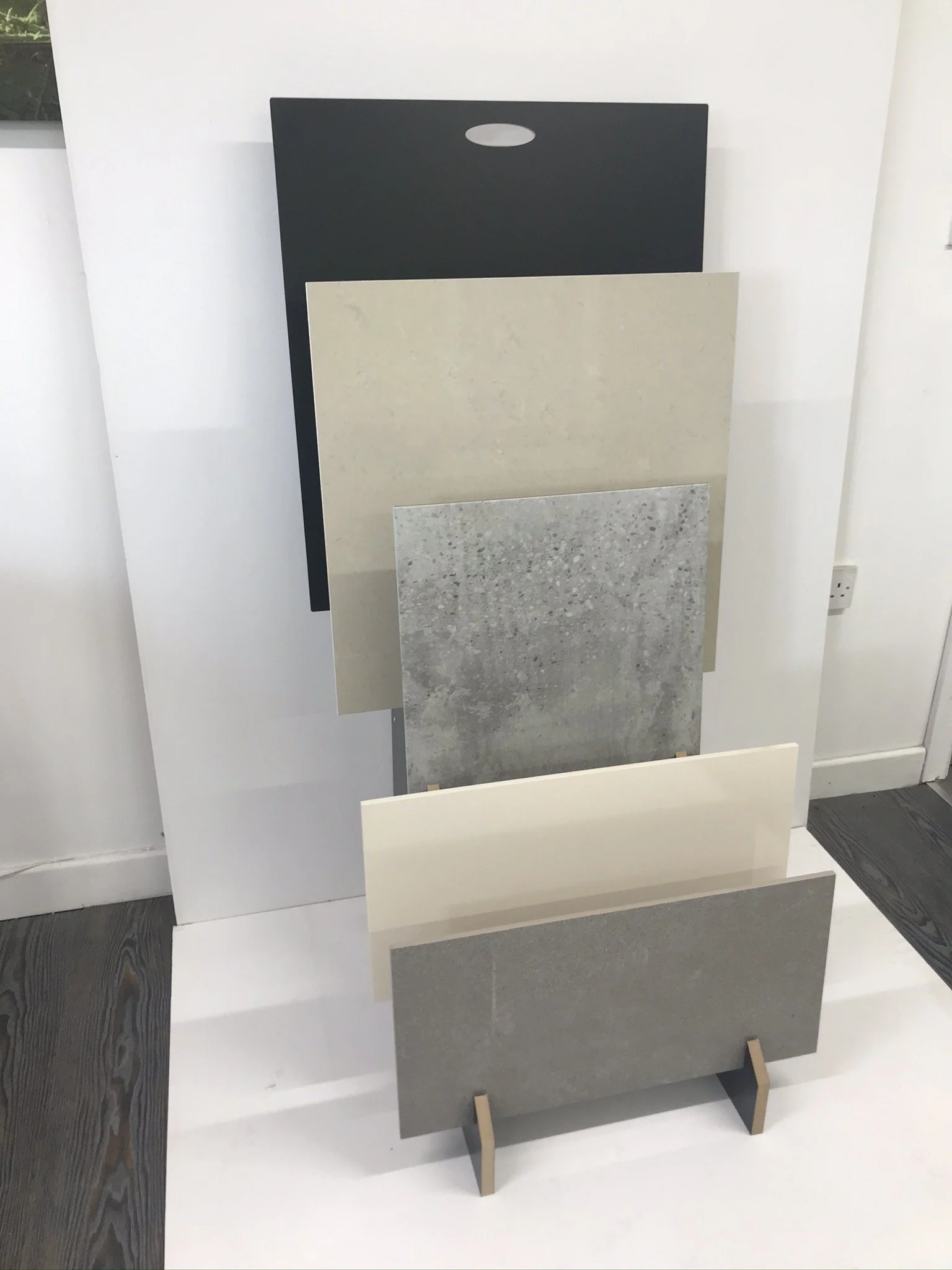Display of various flooring and wall tile samples in neutral colors on stands against a white background.