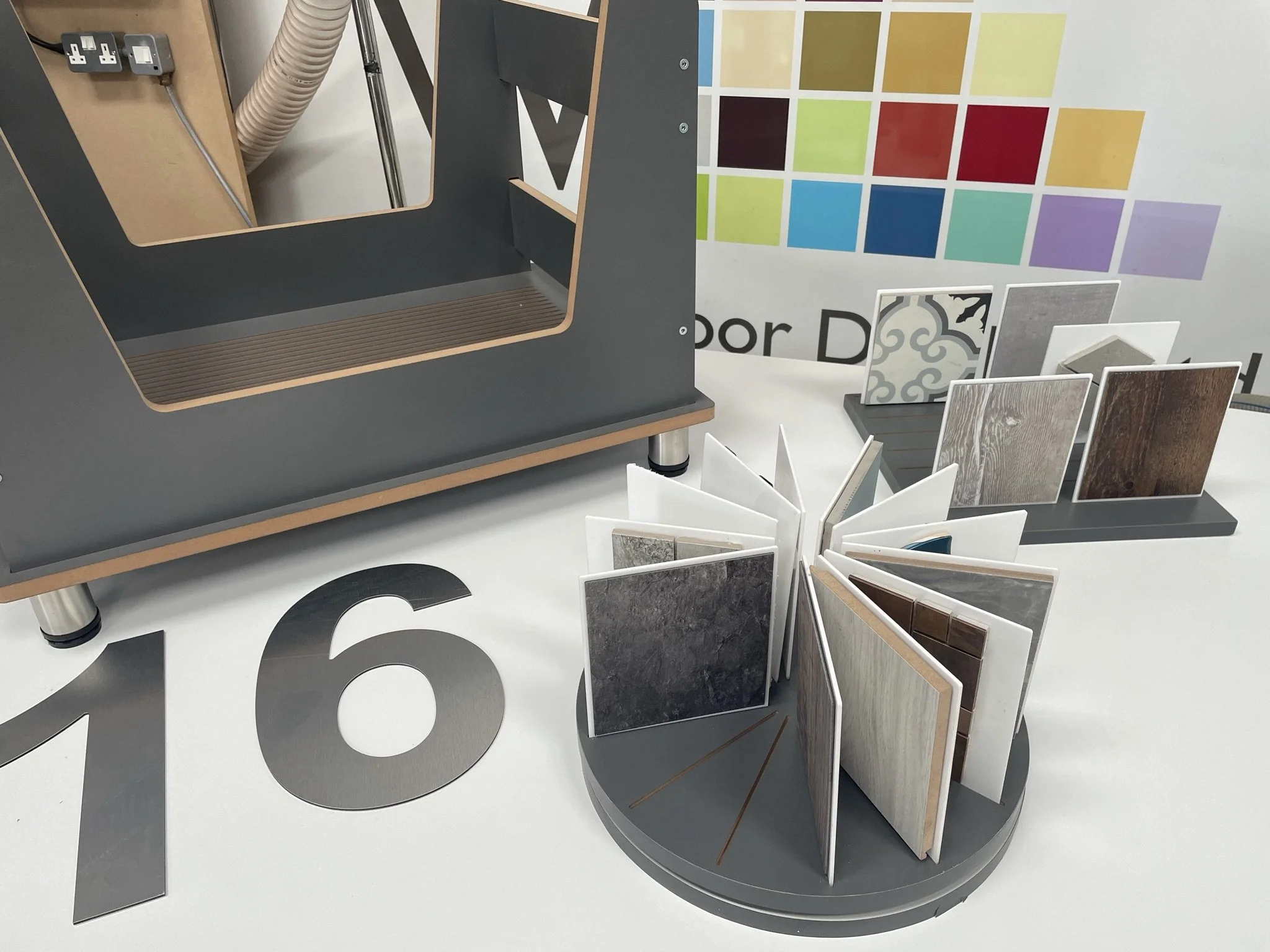 Display of laminate flooring samples with color palette on wall, industrial machine part, and large number 16 on surface.