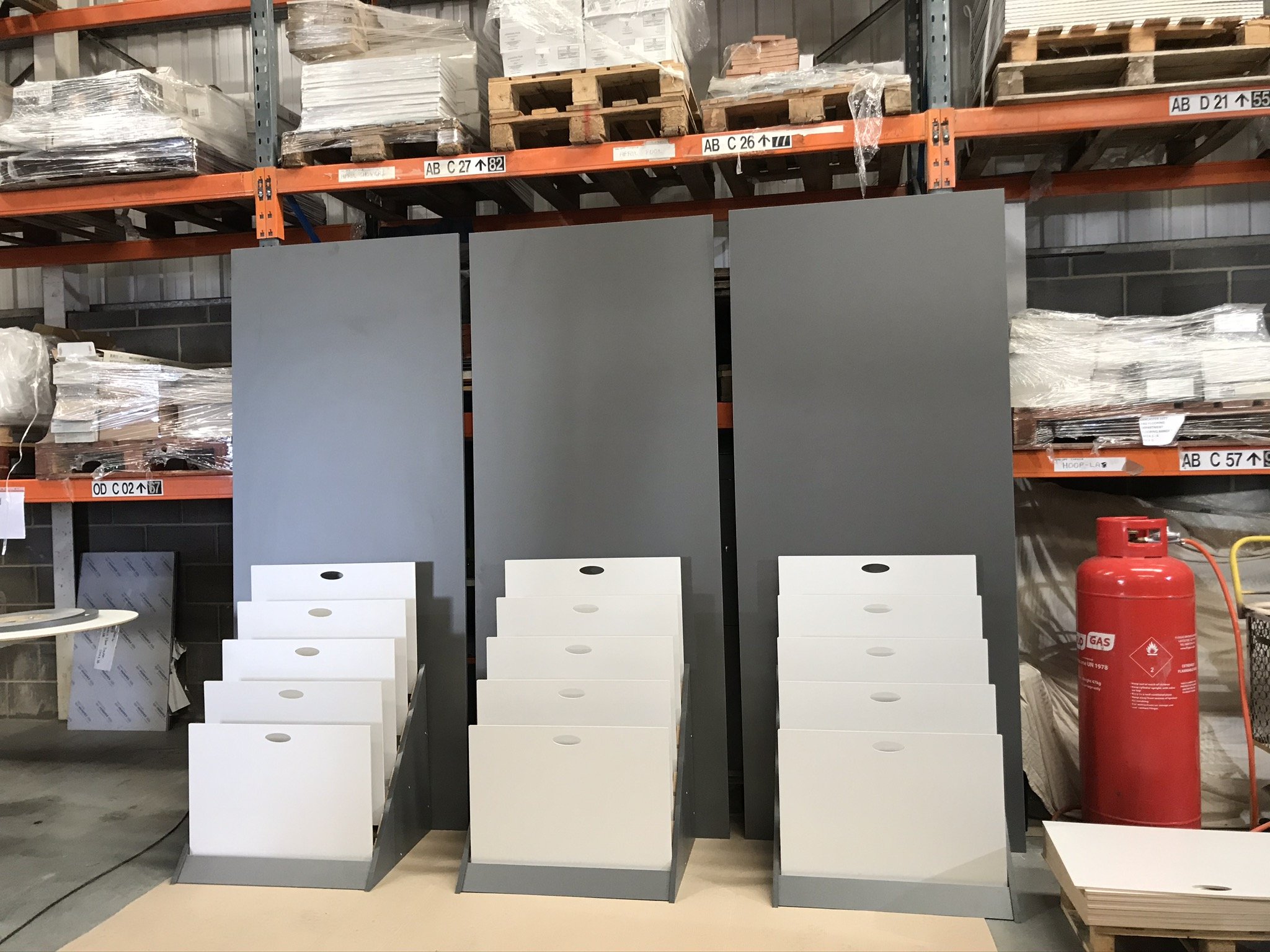 Warehouse shelves with stacked materials, white panels, and a red gas cylinder.
