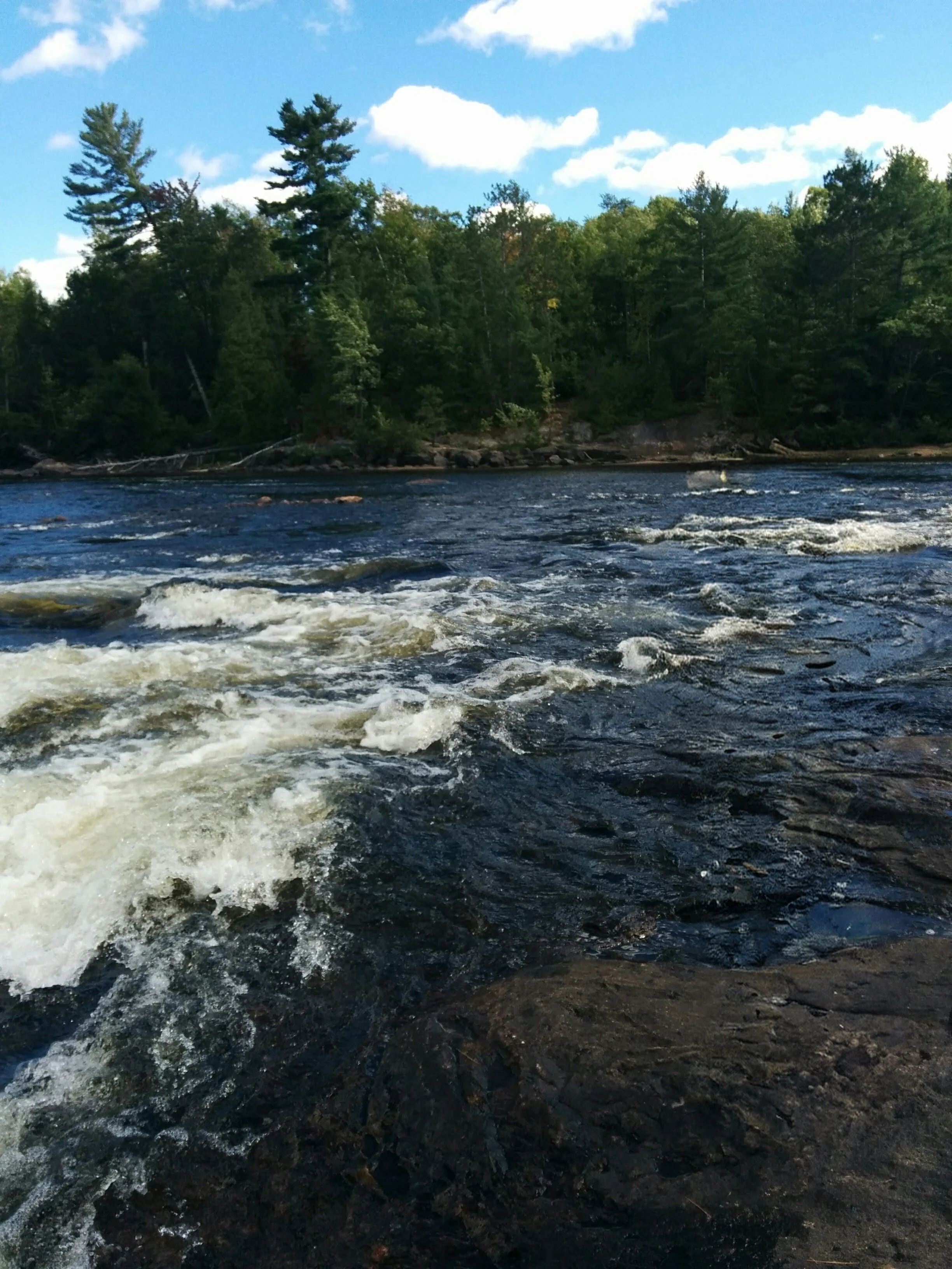 River with rocks and trees along the bank, blue sky with some clouds.