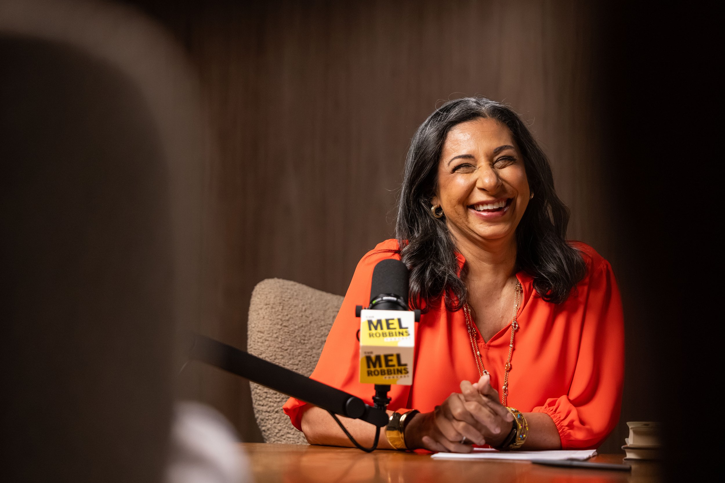 Dolly Chugh sitting at a desk in front of a microphone for the Mel Robbins podcast