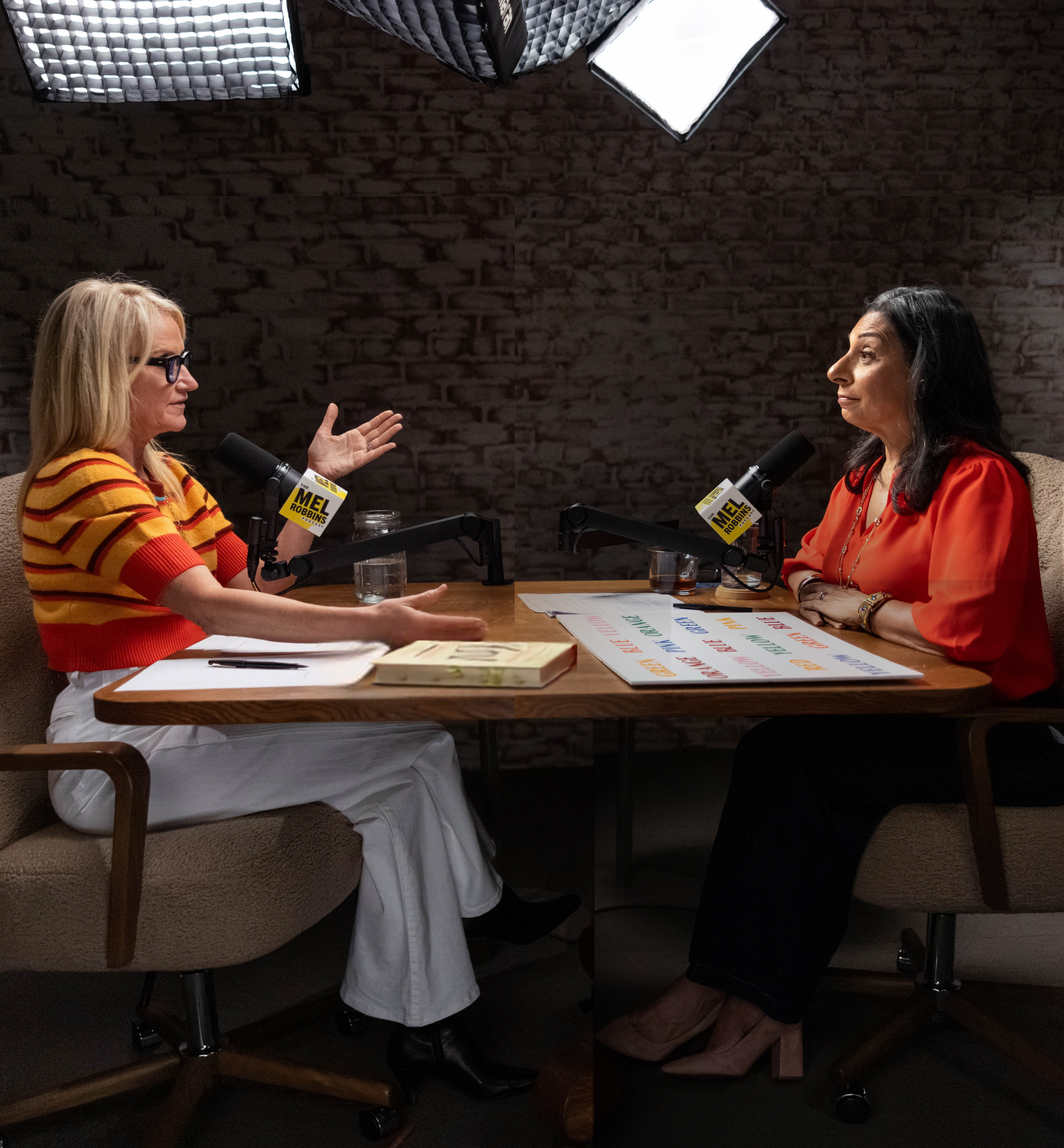 Dolly Chugh and Mel Robbins sitting at a desk recording for the Mel Robbins Podcast