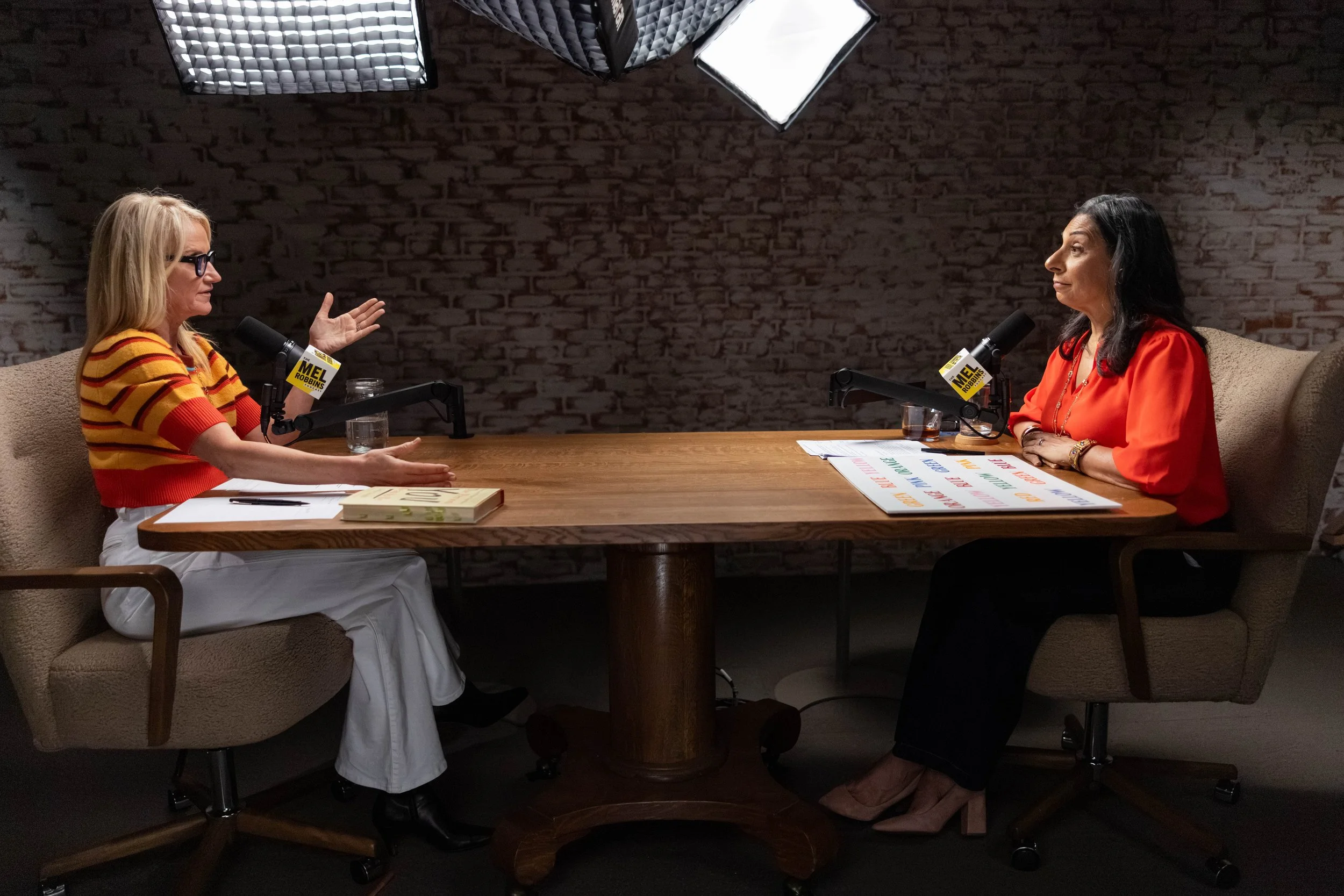 Dolly Chugh and Mel Robbins sitting at a desk recording the Mel Robbins Podcast