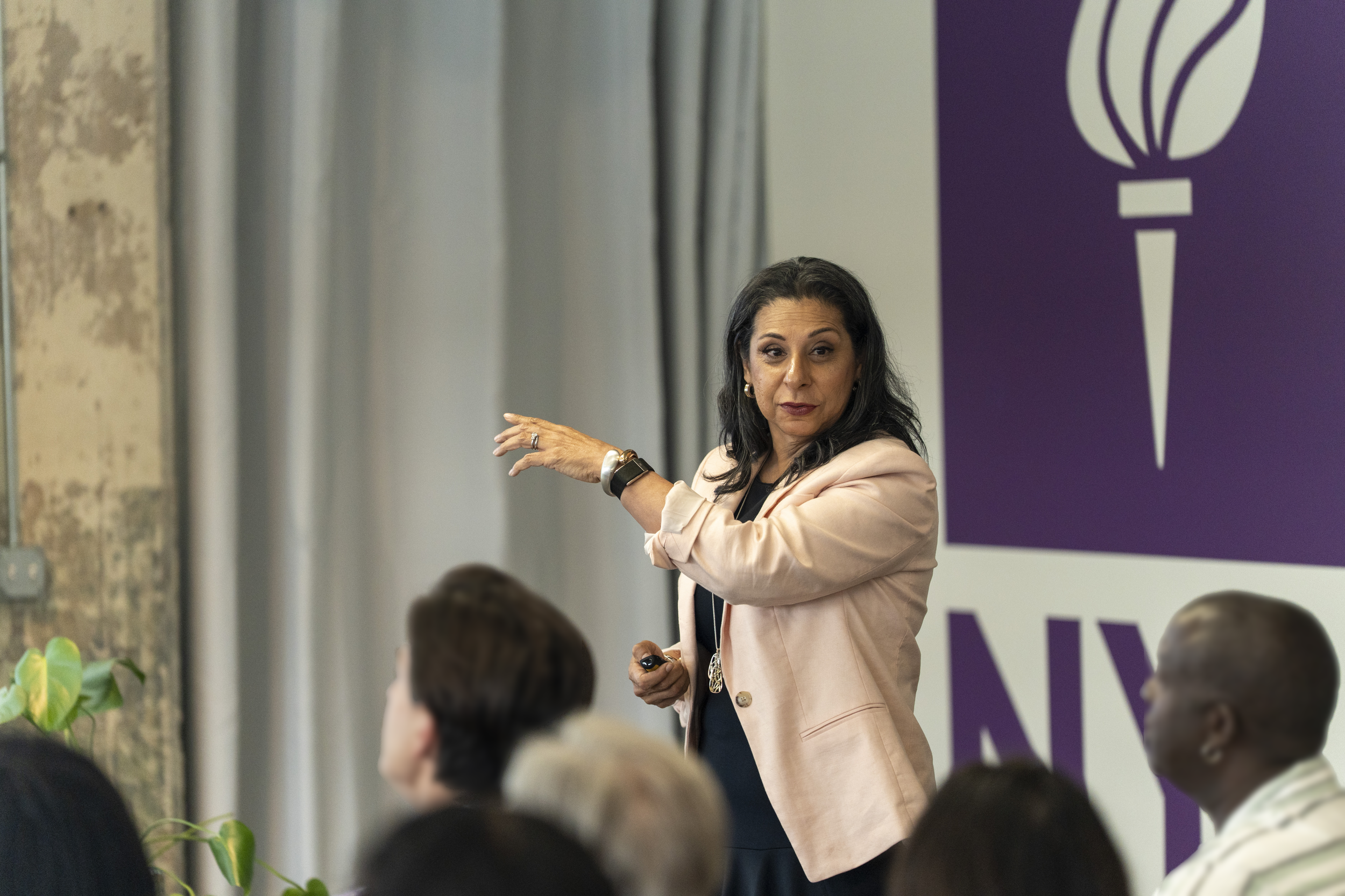 A woman with black hair is presenting in front of a group of people.