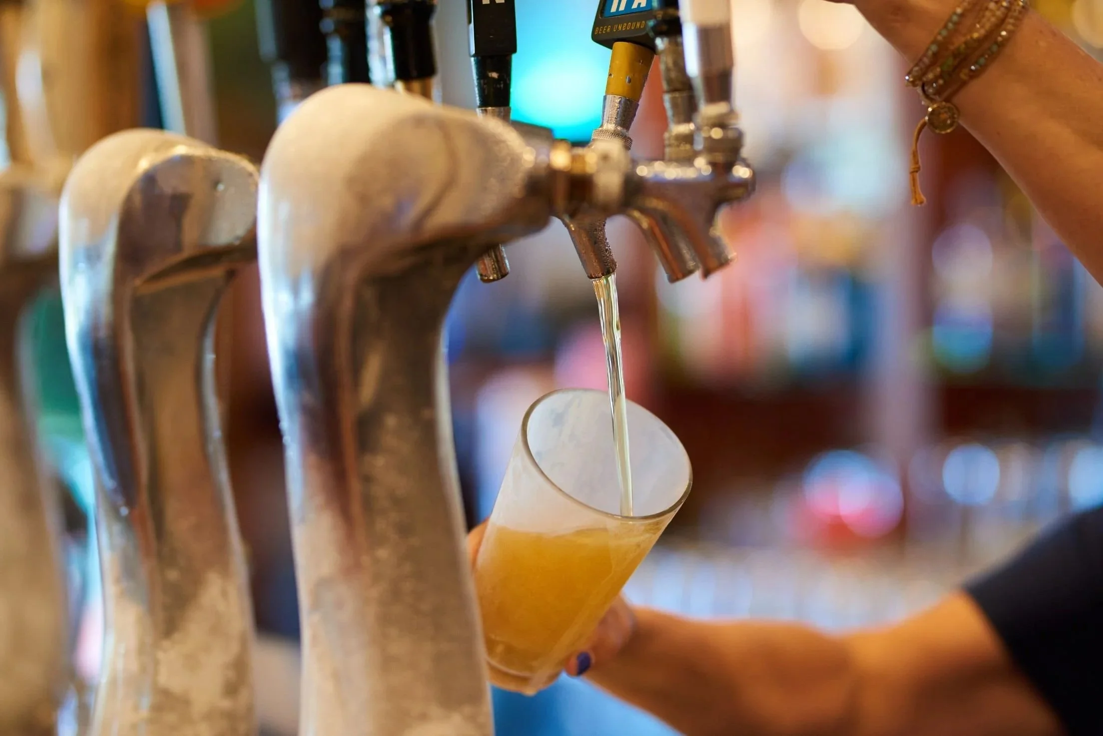 Close-up of beer taps in a bar with a person's hand pulling one of the taps and pouring beer into a glass.