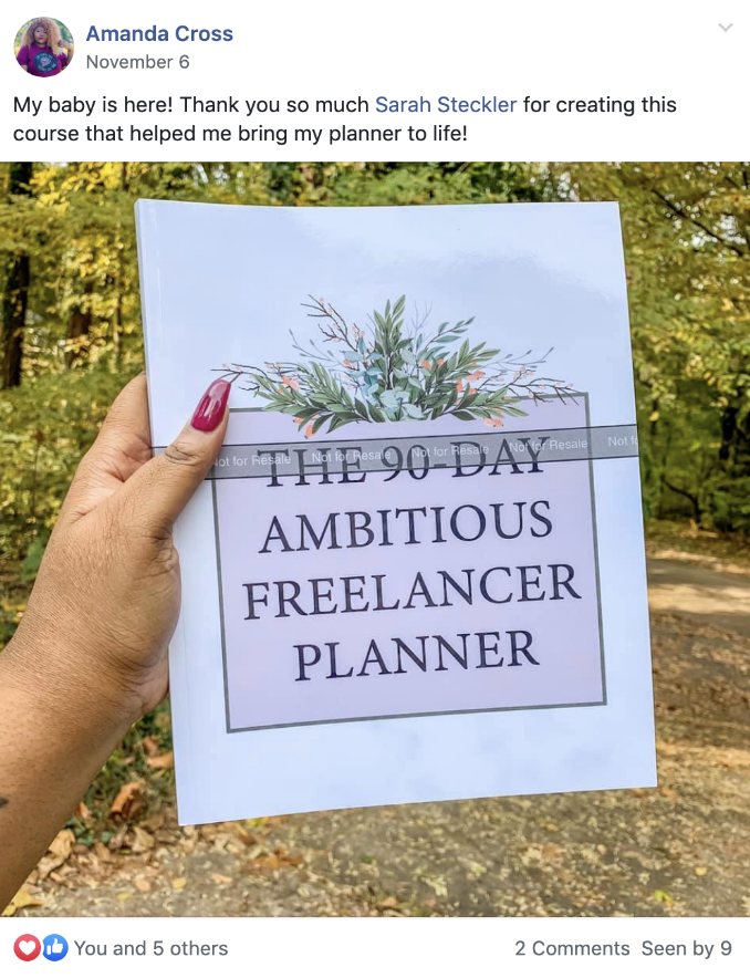 Hand holding a printed freelance planner titled 'The 90-Day Ambitious Freelancer Planner' outdoors with trees and fallen leaves in the background.