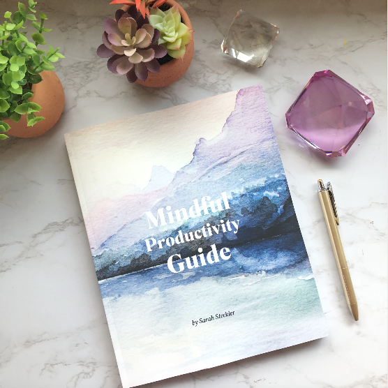A book titled "Mindful Productivity Guide" by Sarah Stedker on a marble surface, surrounded by potted succulents, a glass paperweight, a purple faceted crystal, and a gold pen.