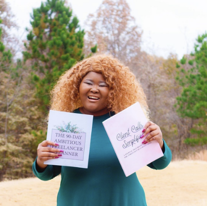 A woman with curly, blonde hair smiling outdoors, holding two papers with text.