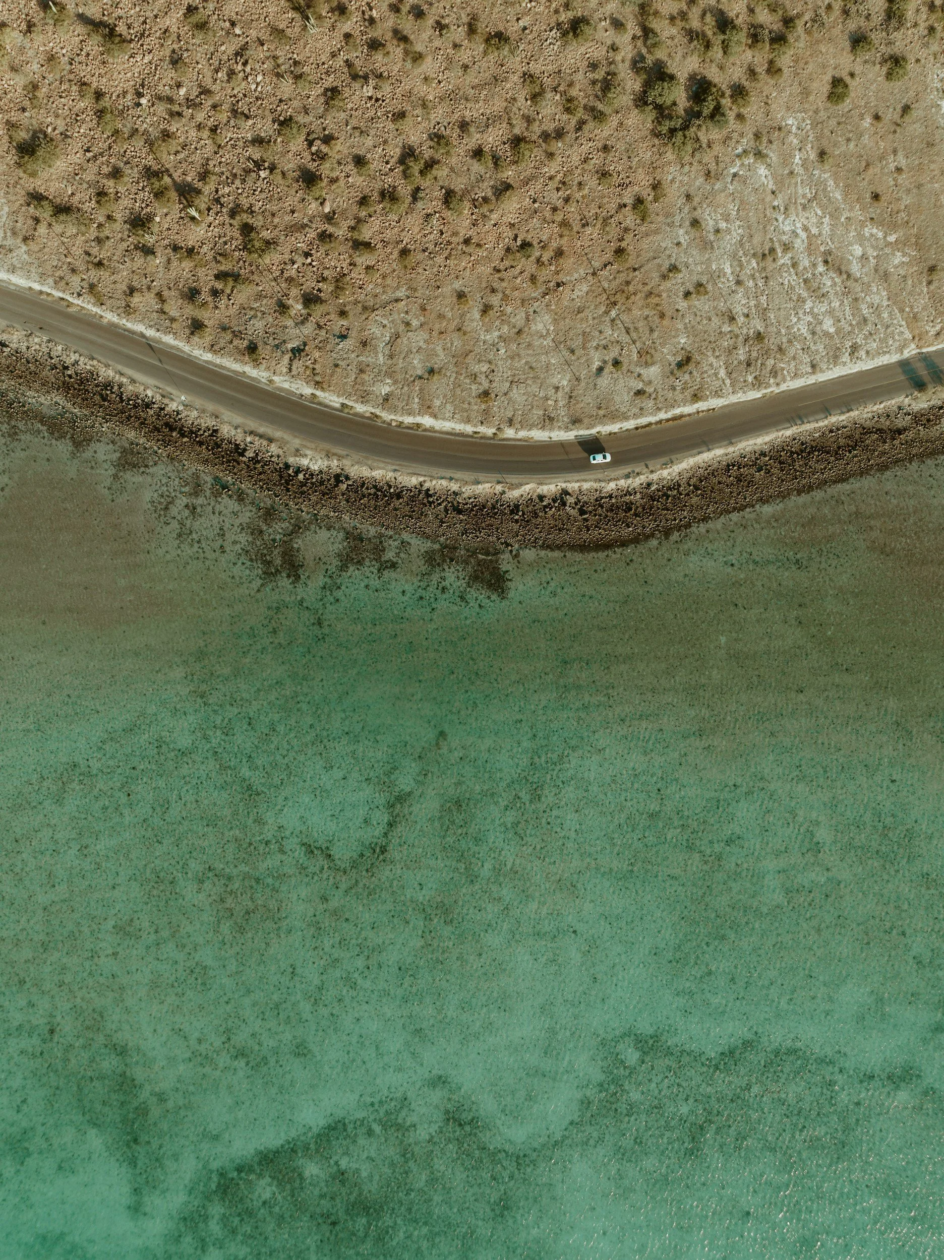 An aerial view of a winding road running along a green and dry terrain.