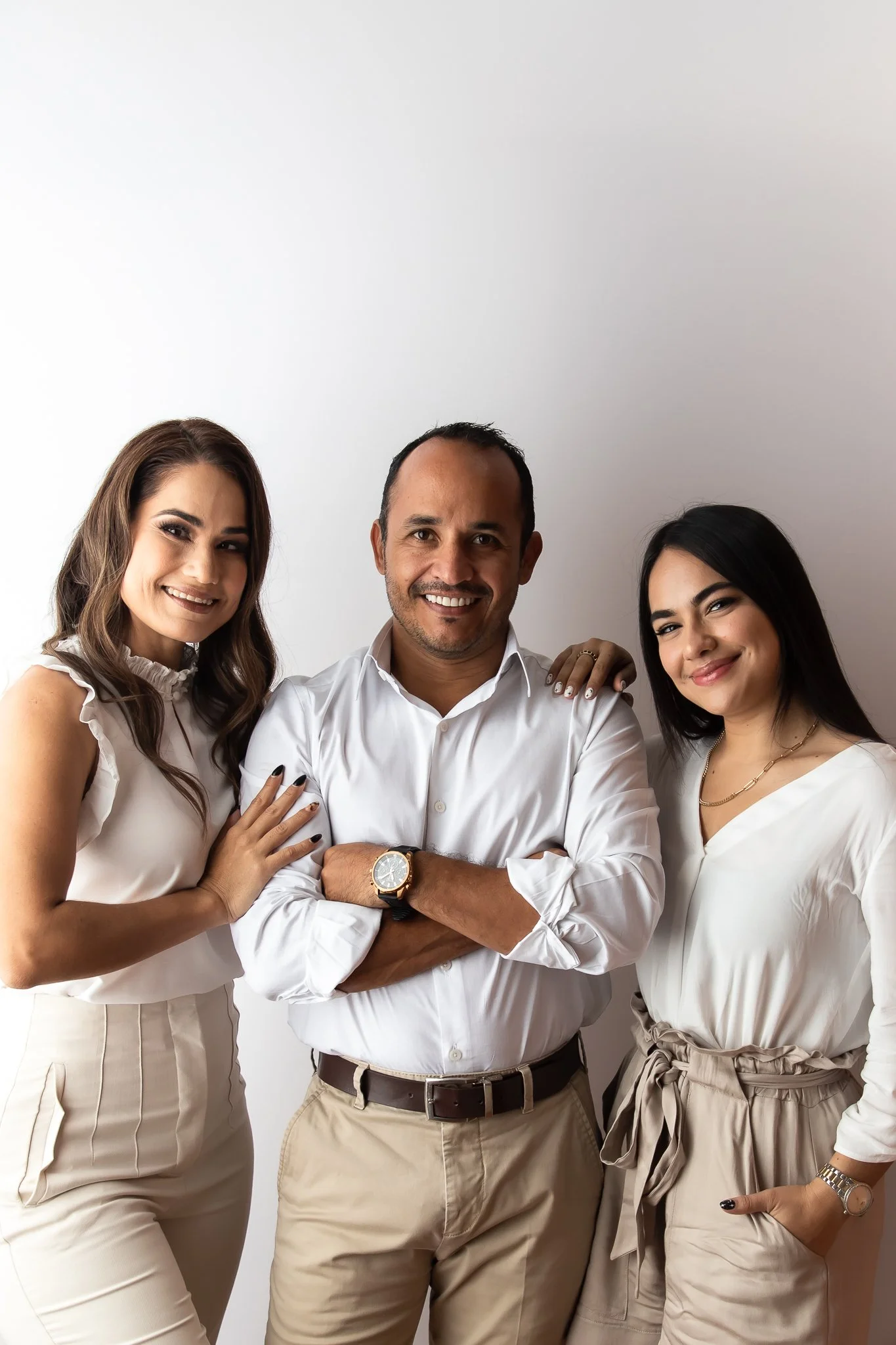 Three people standing close together against a light background, smiling at the camera. The man in the center has his arms crossed. Two women stand beside him, one on each side.