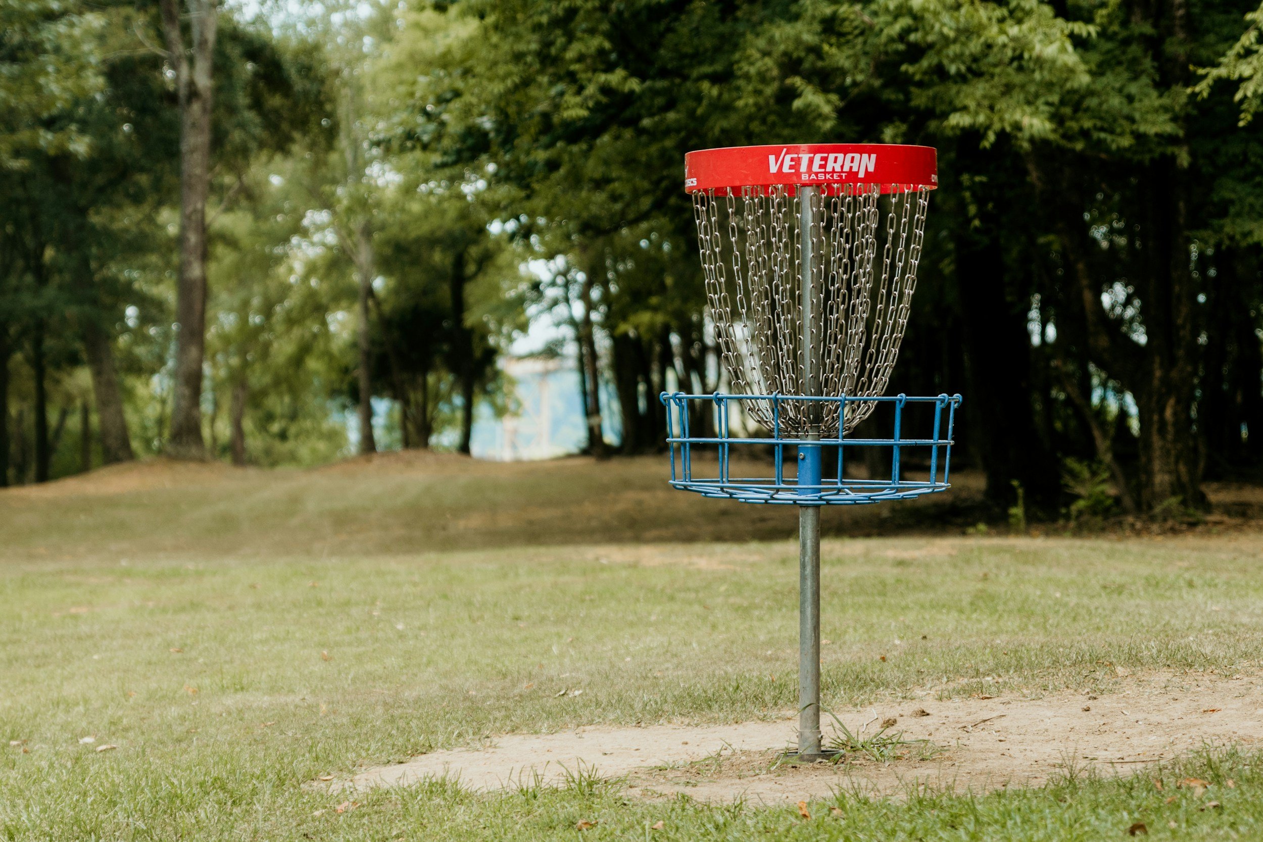 A disc golf basket stands alone on a grassy area with trees in the background.