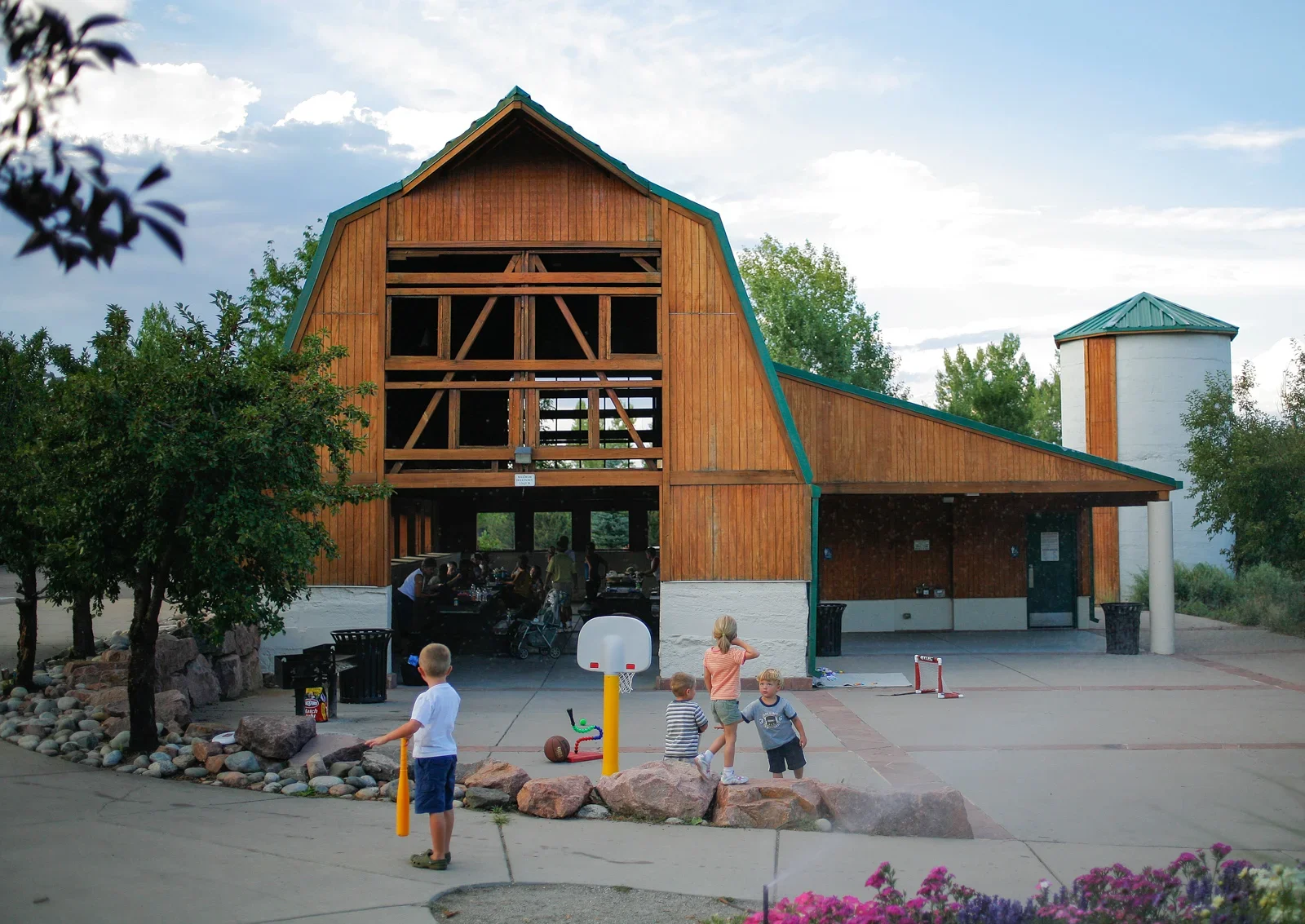 Children playing outside of a large mountain lodge-style building with people inside and trees around, under a partly cloudy sky.
