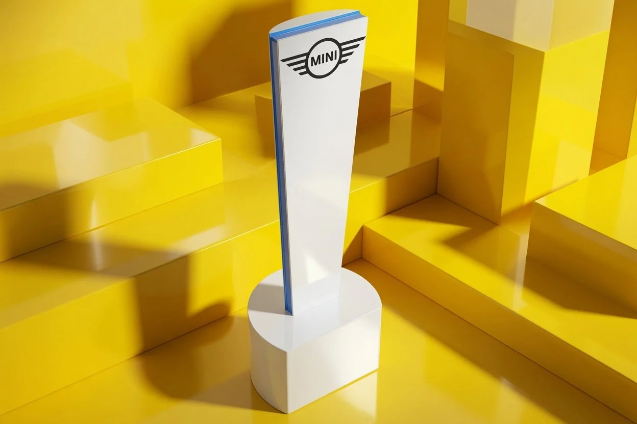 A custom corporate award of the Mini Cooper logo on a tall white stand on a yellow stage with yellow walls and steps.