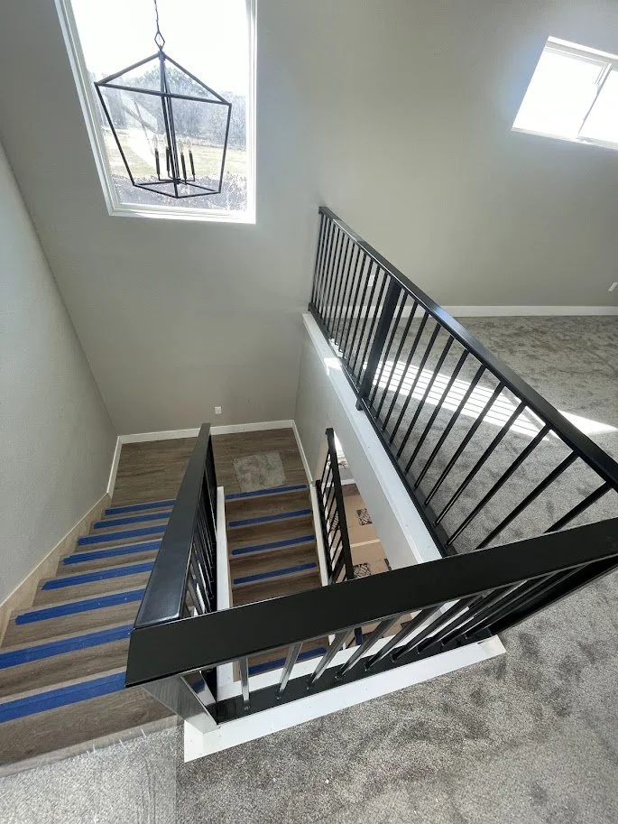 View of a staircase and landing in a modern home, with a black metal railing, a large window, and a pendant light fixture hanging from the ceiling.