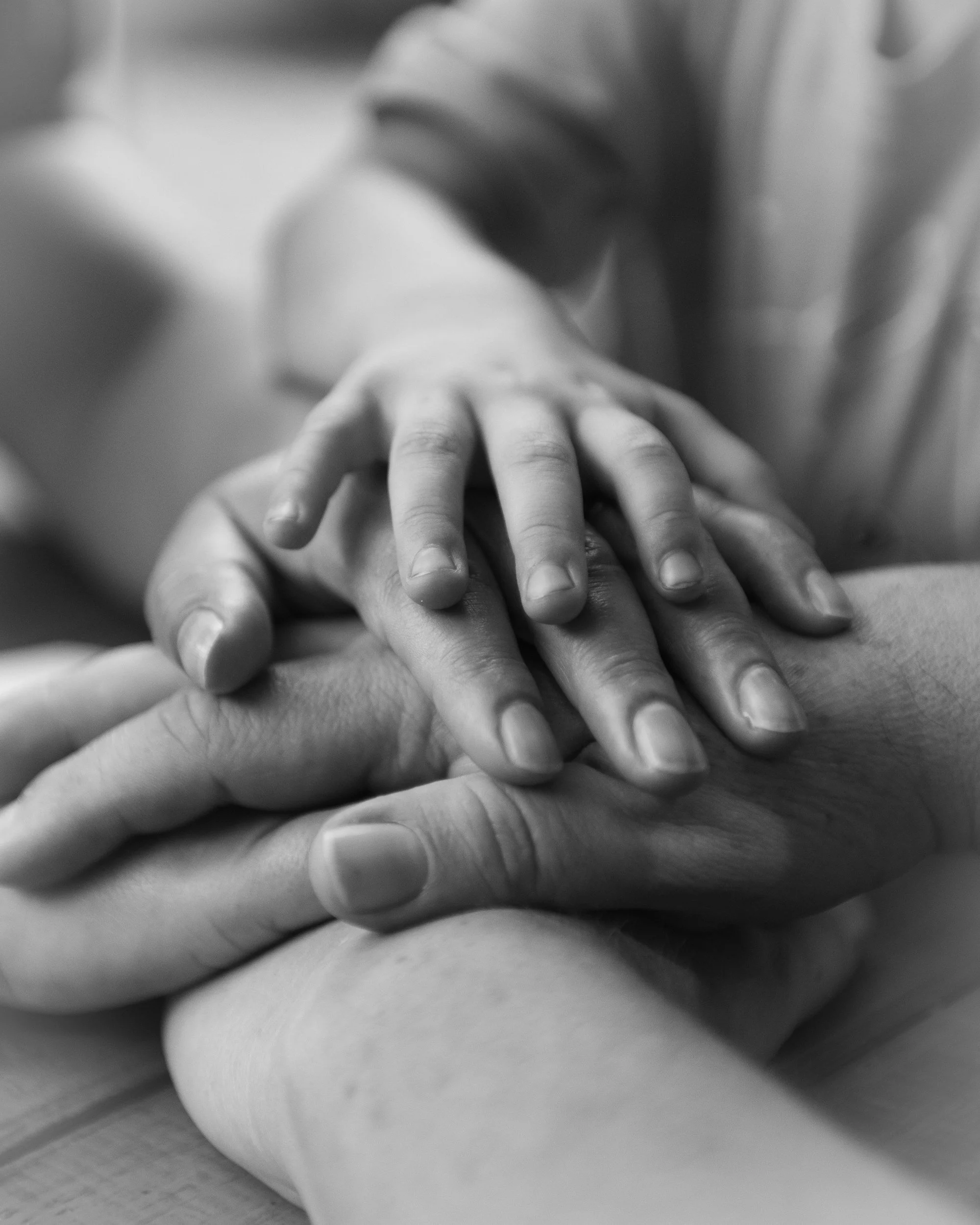 Close-up black and white photo of a child's hand resting on an adult's hand, symbolizing protection or connection.