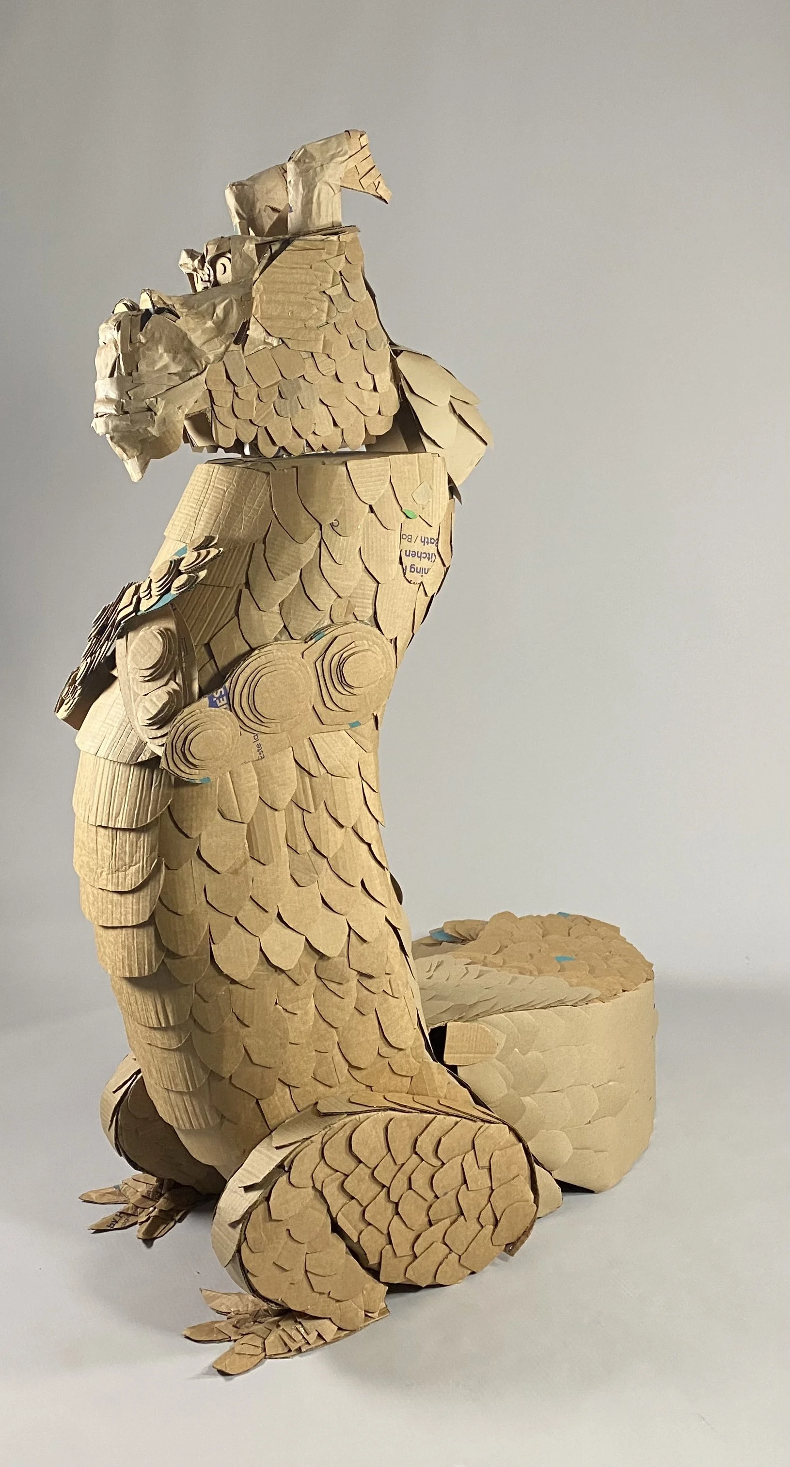 A sculpture of a dragon made from cardboard, featuring detailed scales, horns and tail.