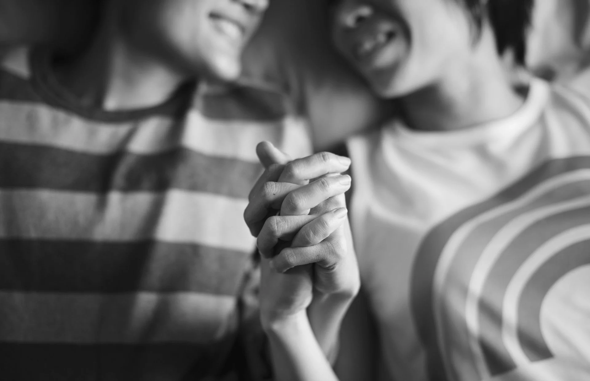 Two women with smiles holding hands in a prayer position, wearing casual striped shirts.