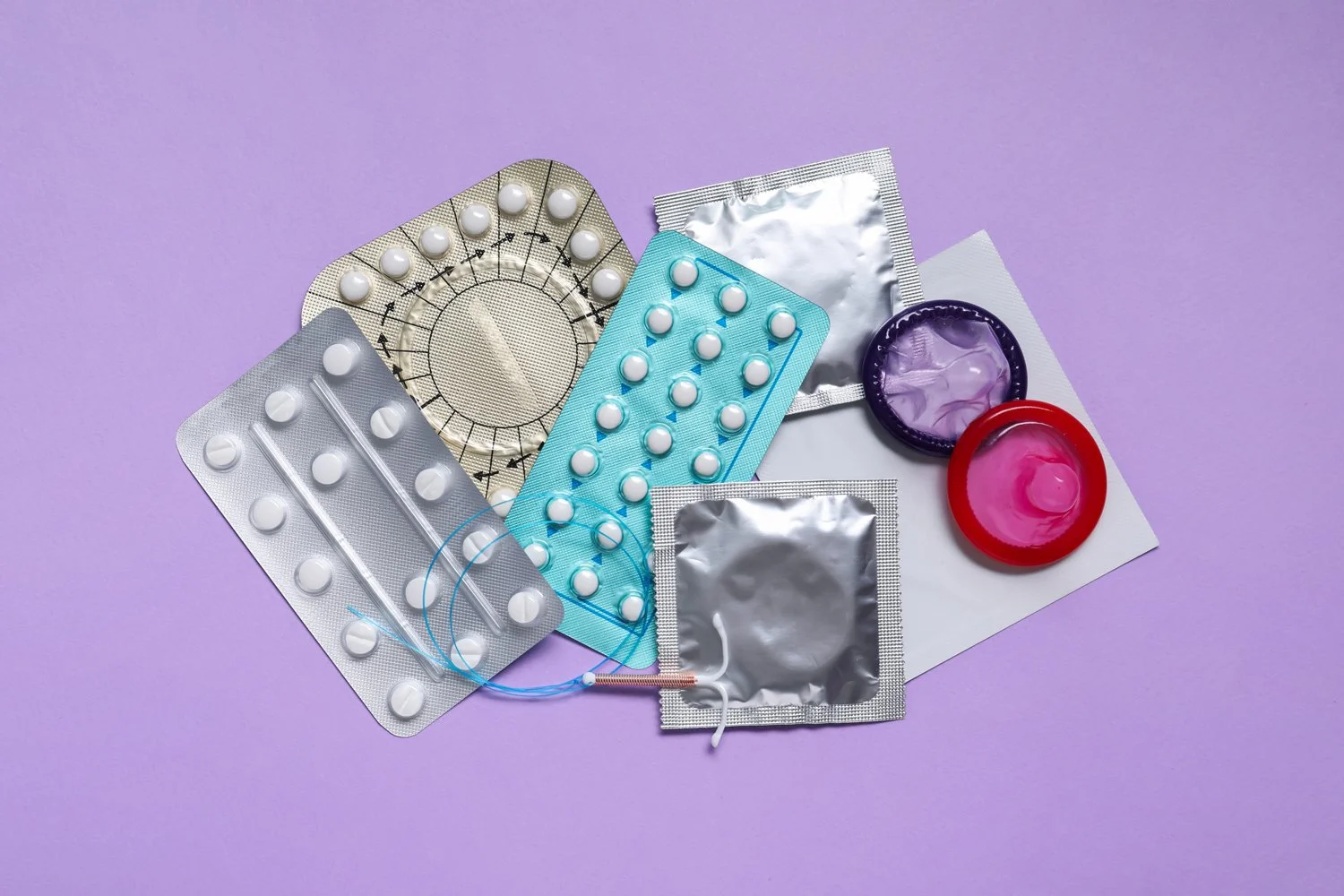 Various contraceptive devices on a purple surface, including blister packs of pills, diaphragms, and open contraceptive cases.