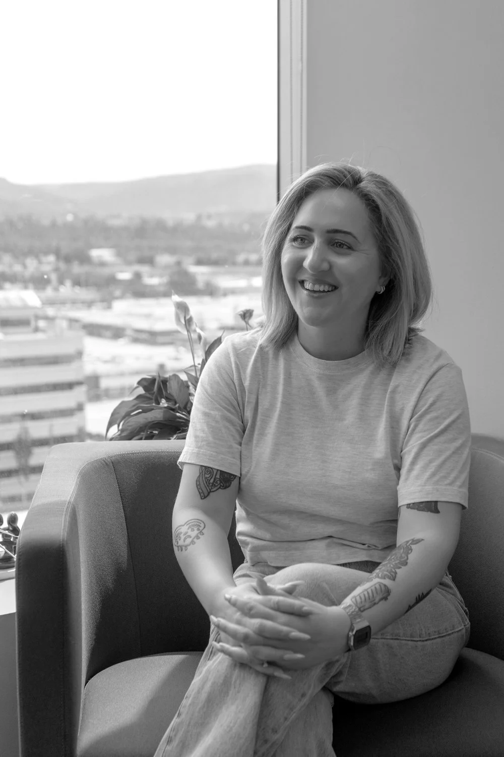 Lucy Snider sitting on a chair near a window, smiling, indoors with a mountain view outside.