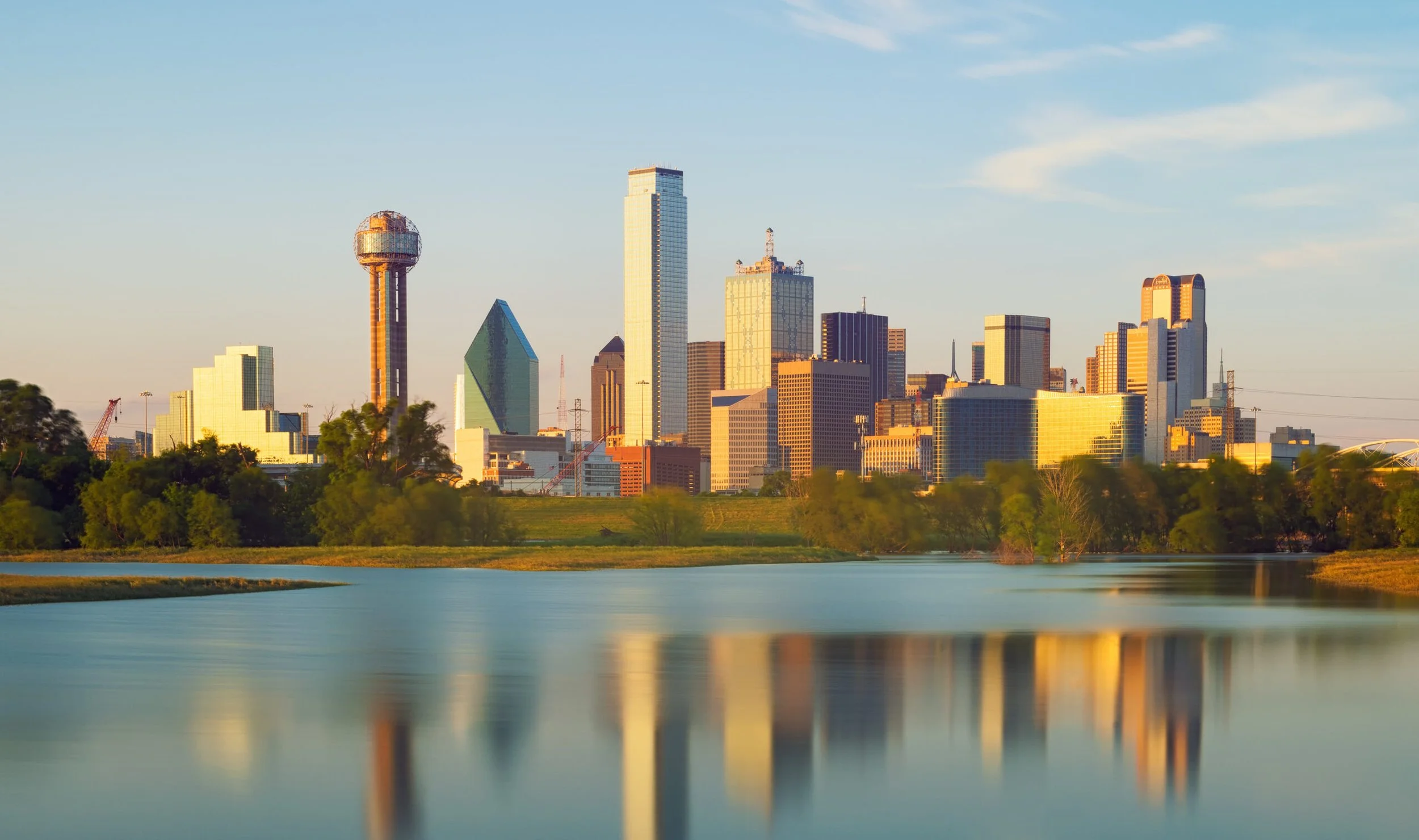 Dallas skyline with tall modern skyscrapers reflecting in a calm body of water at sunset.
