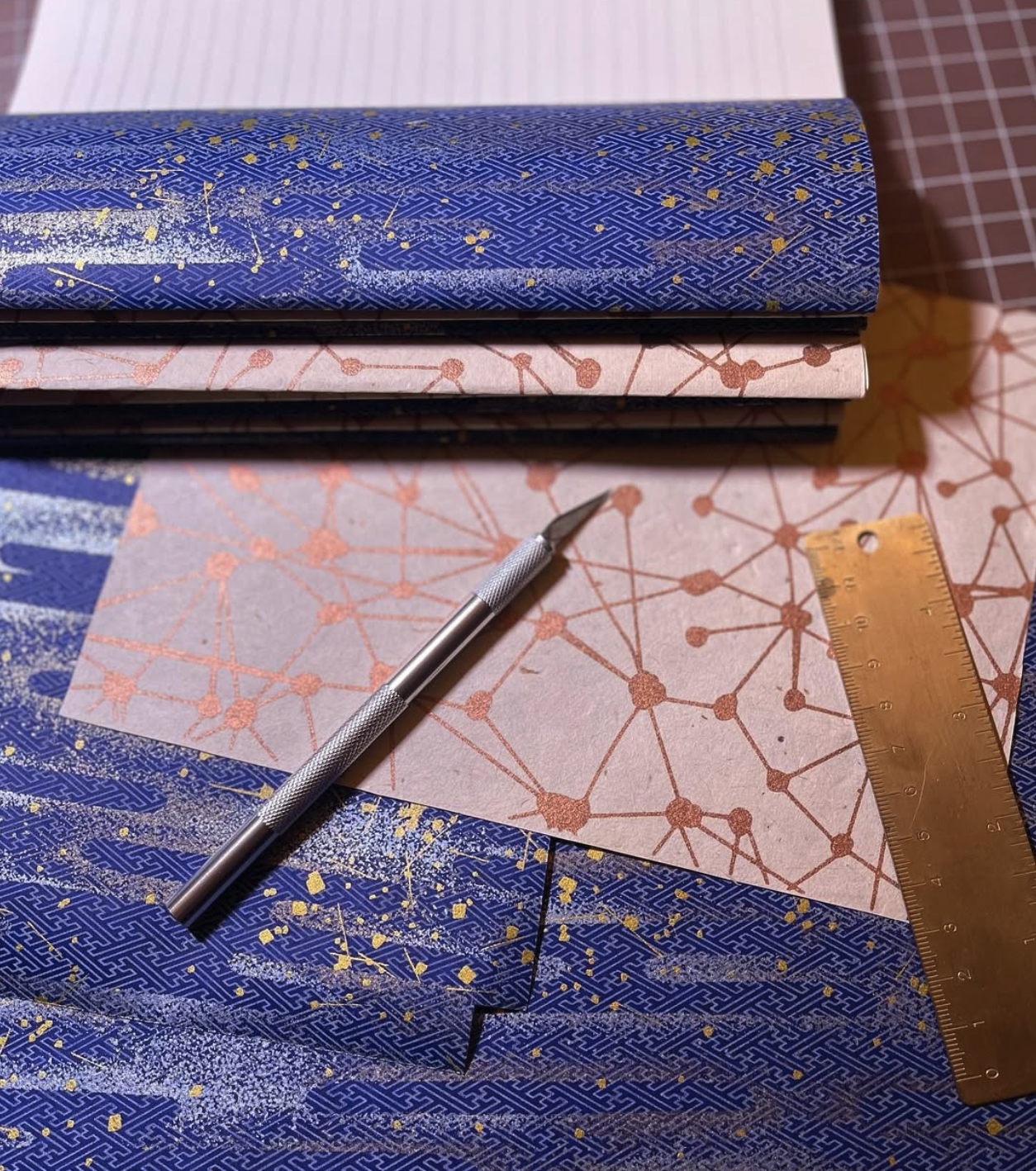 Close-up of a workspace with colorful patterned papers, a metal craft knife, and a wooden ruler.