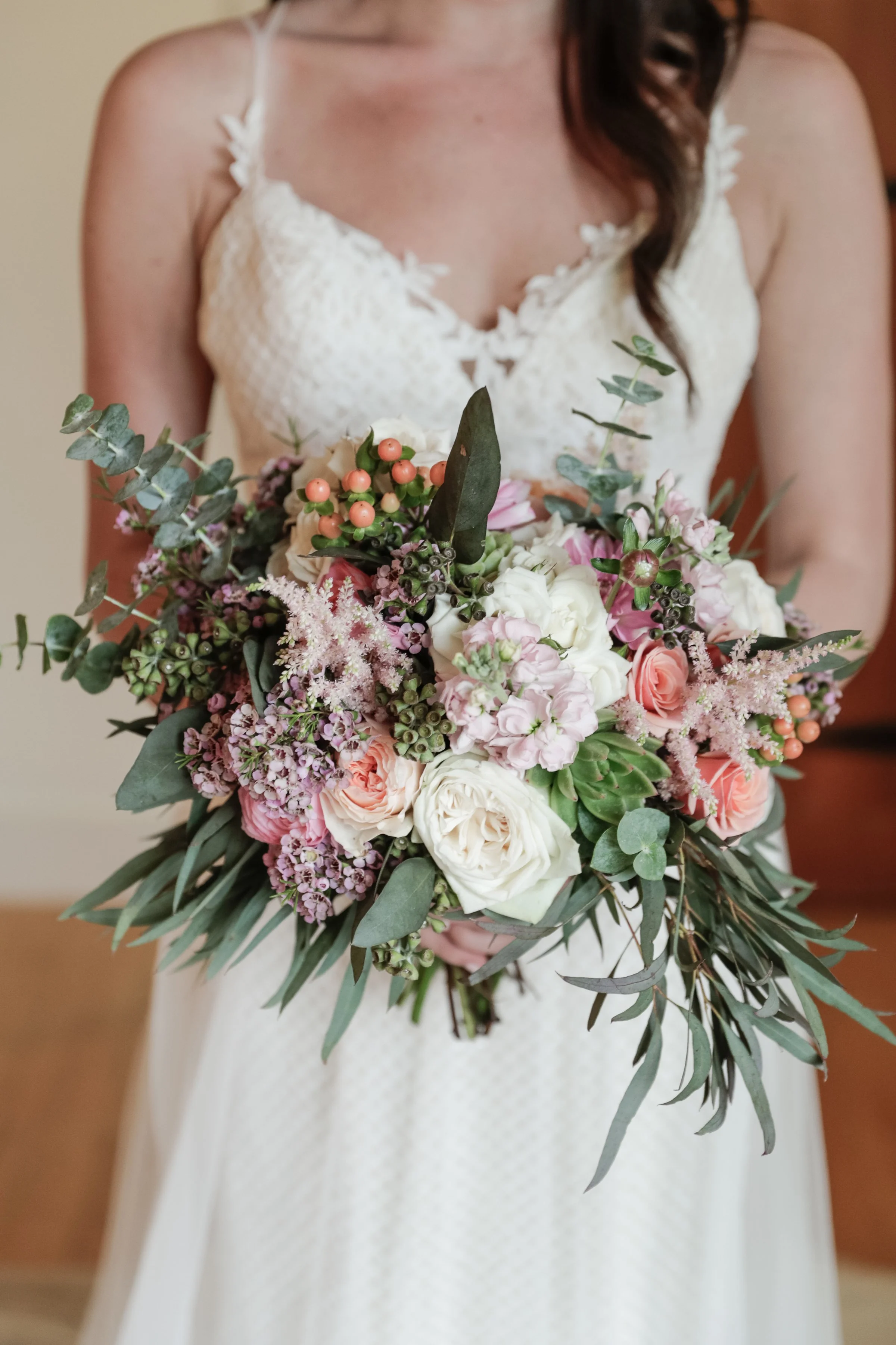 A woman in a white dress holding a bouquet of flowers, including pink roses, white flowers, greenery, and berries.