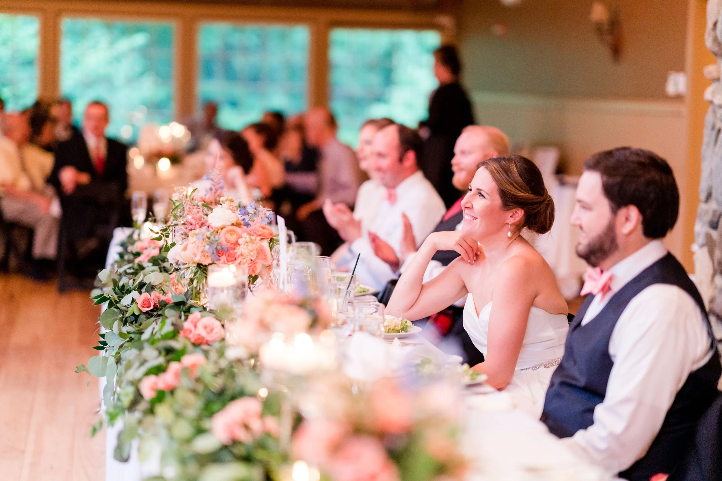 Guests seated at a wedding reception table decorated with pink and peach flowers, enjoying the celebration.