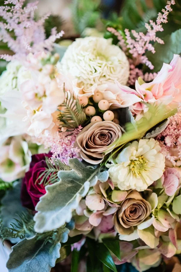 Close-up of a bouquet of assorted flowers including roses, hydrangeas, and greenery in pastel and rich colors.