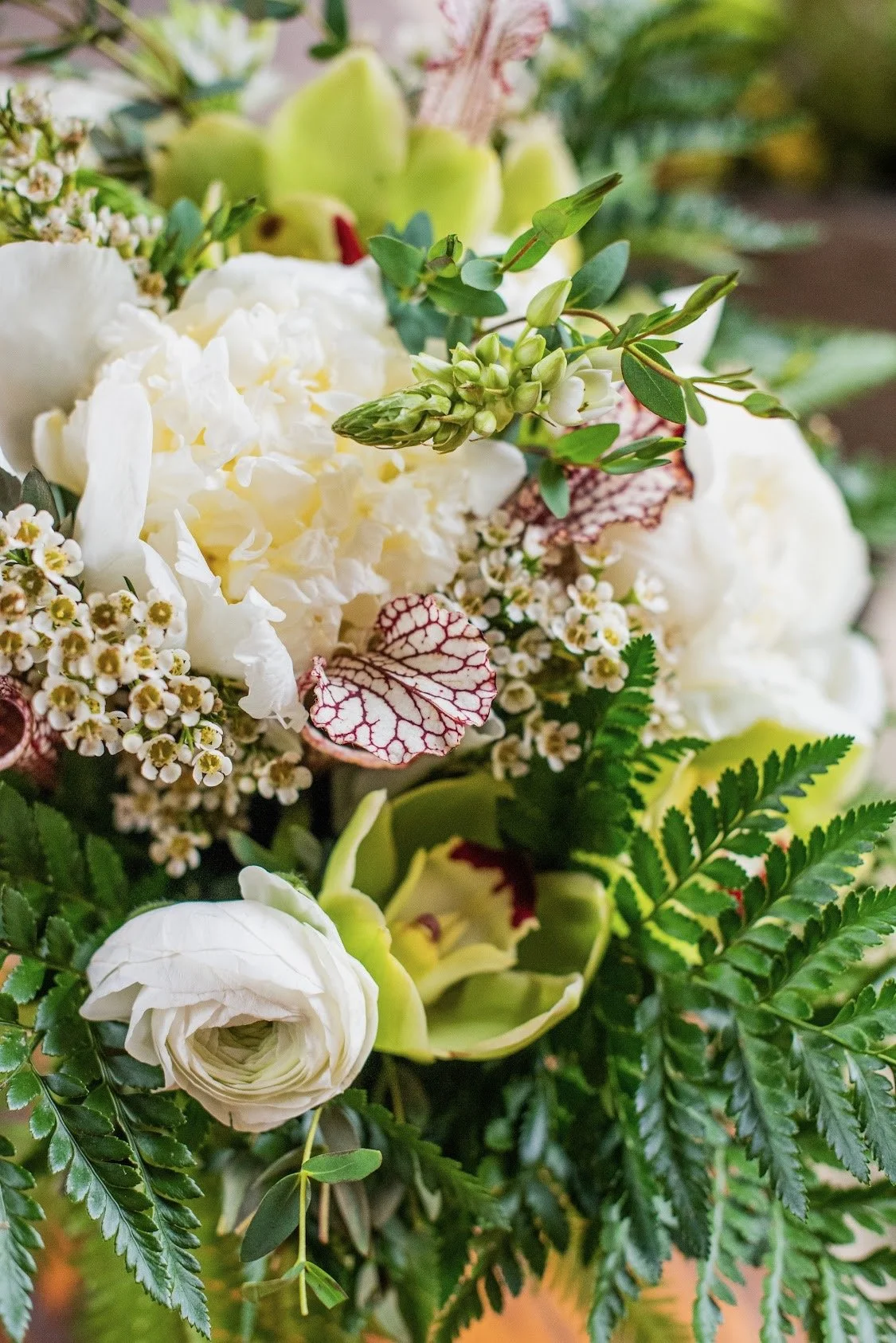 Close-up of a floral arrangement with white hydrangeas, white roses, small white and yellow flowers, green foliage, and pink-veined leaves.